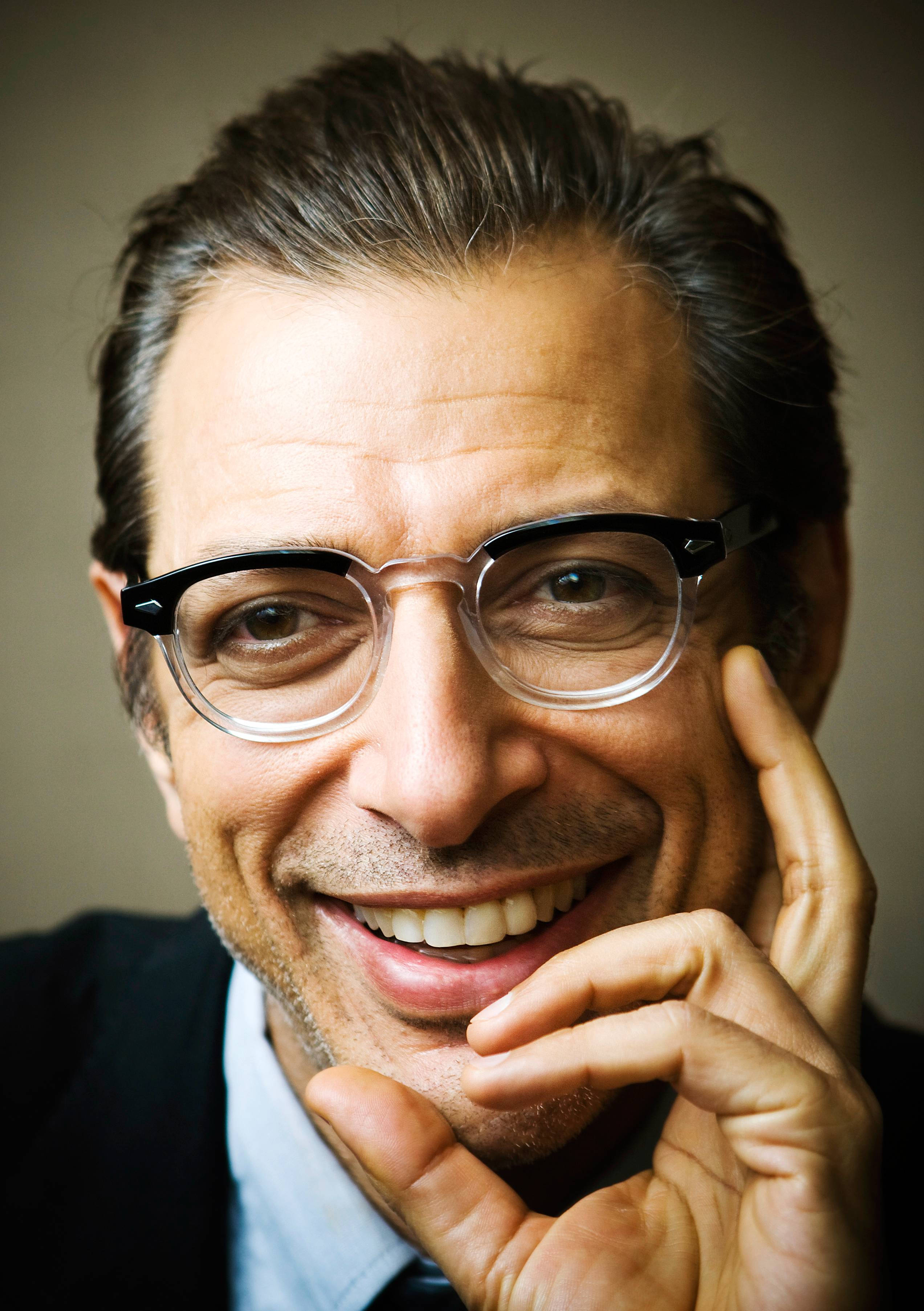 Celebrity 桌布 壁紙 — 一個戴眼鏡微笑的男人，將下巴擱在手上，靠著中性背景的特寫肖像。
