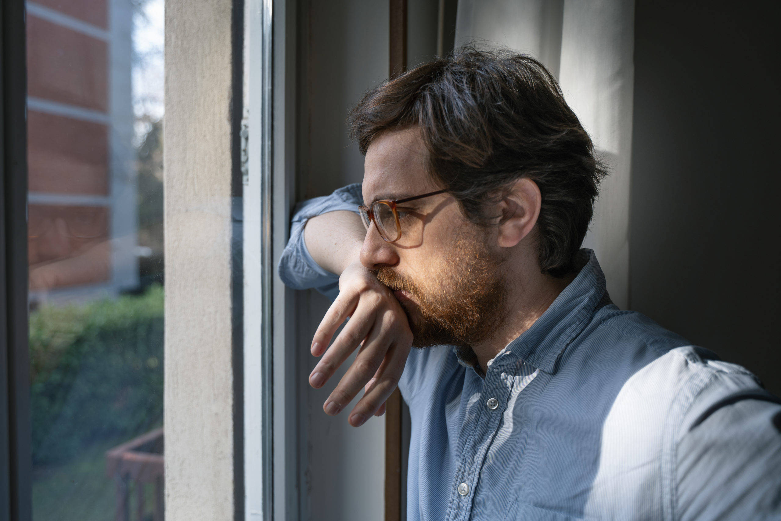 anxious 桌布 壁紙 — 一個戴眼鏡留鬍鬚的男人，用手托著下巴，若有所思地望著窗外。