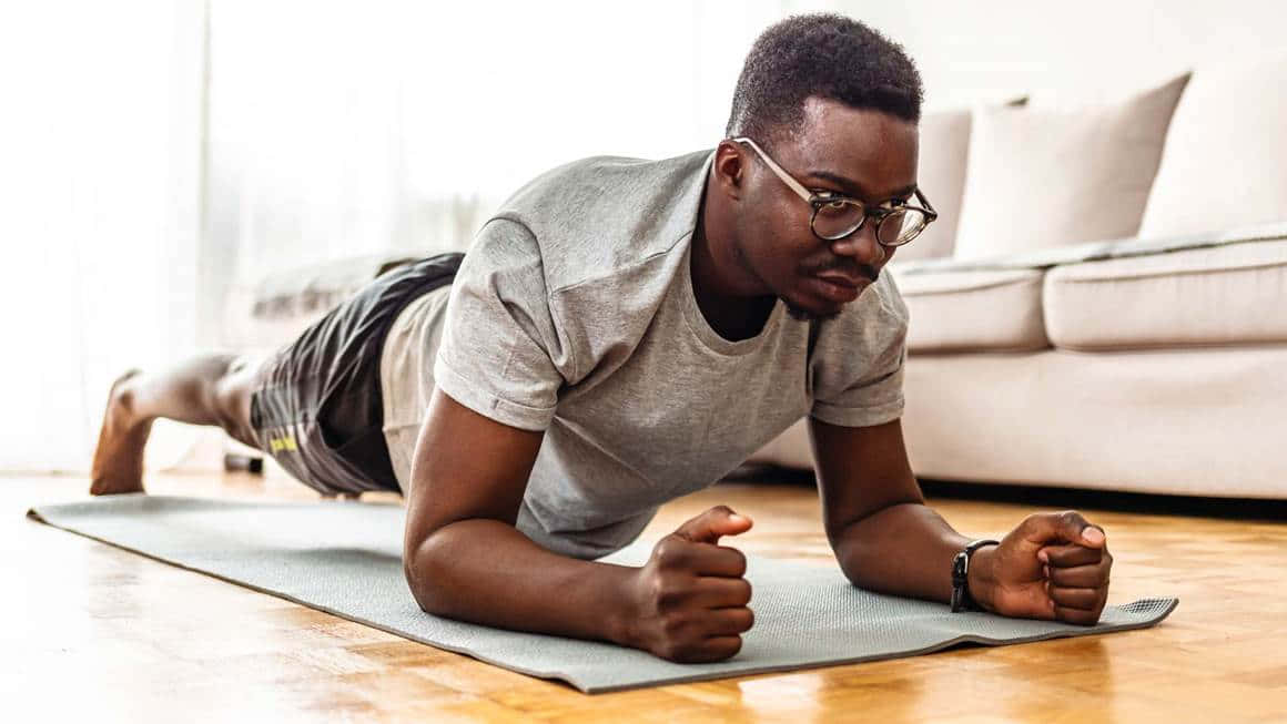 Exercise 桌布 壁紙 — 一個戴眼鏡的專注男子在明亮的現代客廳中的瑜伽墊上保持平板支撐姿勢。