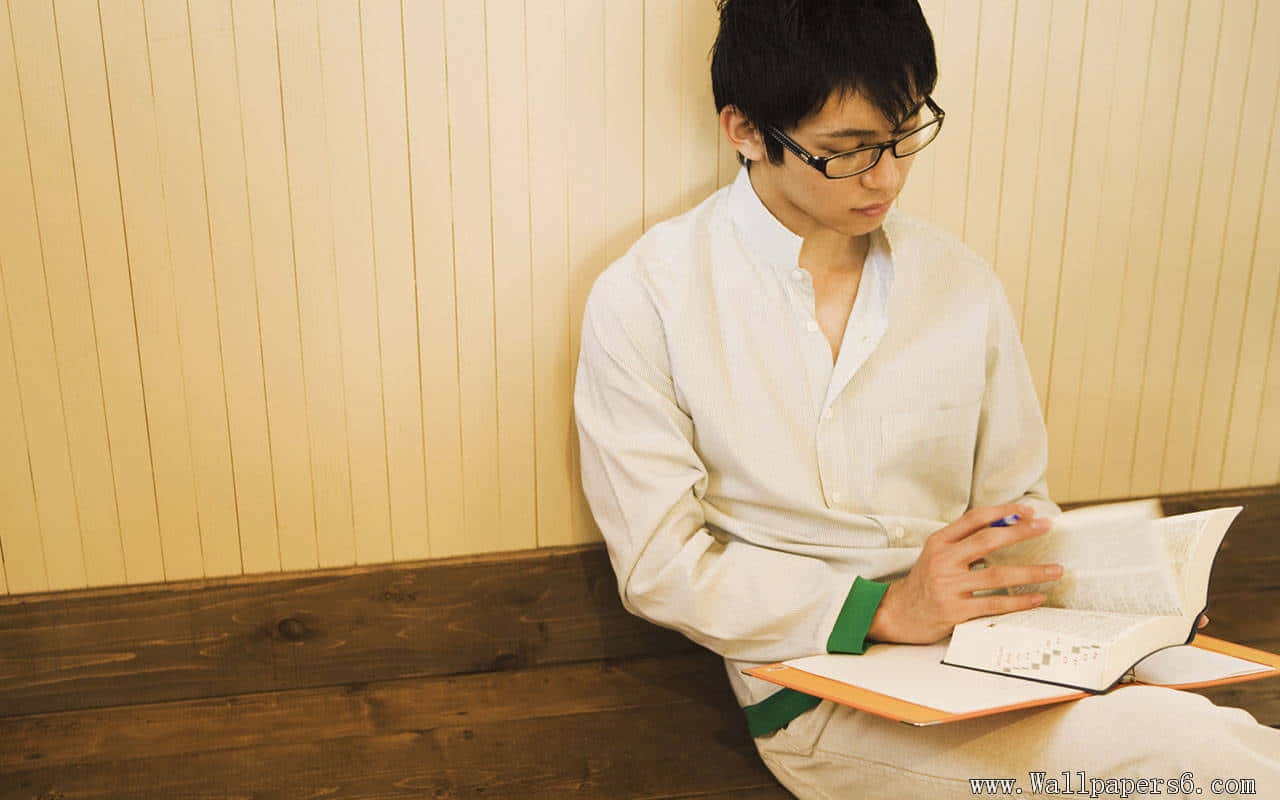 書本 桌布 壁紙 — 一個戴眼鏡的年輕男子坐在木長椅上，靠著溫暖的米色鑲板牆看書。