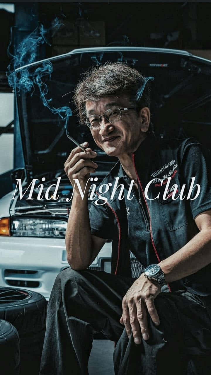 人像動態 桌布 壁紙 — 一個戴眼鏡的男人坐在一輛引擎蓋打開的汽車前，在燈光昏暗的車庫裡抽煙。