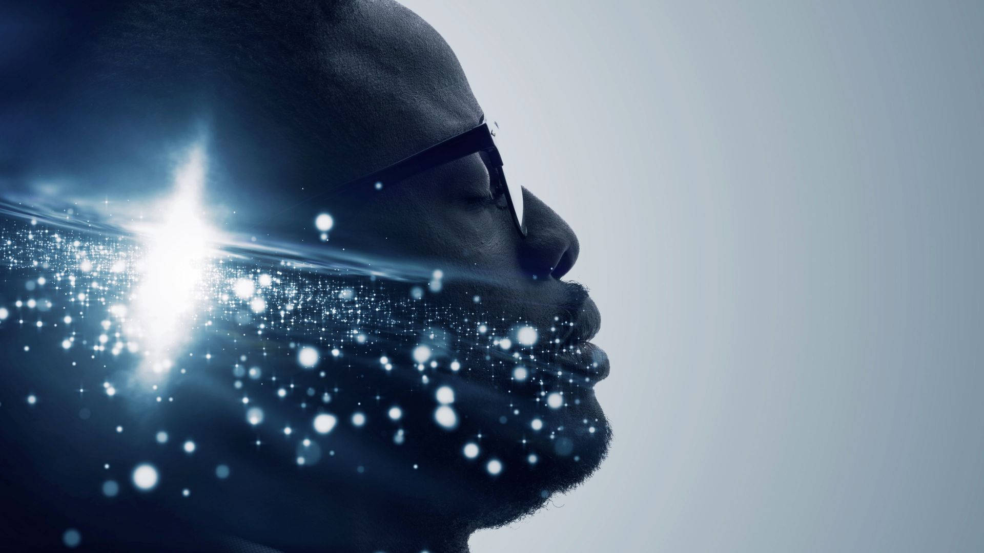 mind 桌布 壁紙 — 一個戴眼鏡的男士側面，他的臉部散發出宇宙粒子和光芒，背景是冷藍色漸變。