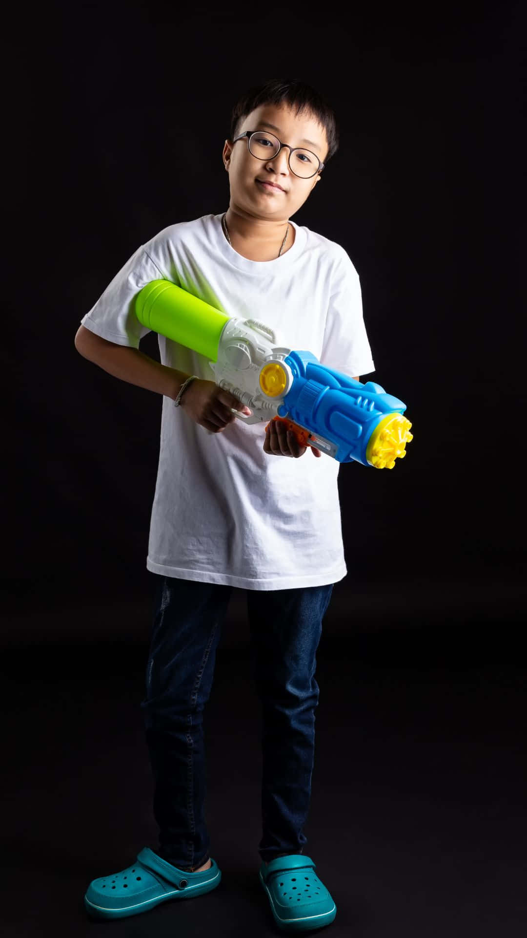 toys 桌布 壁紙 — 一個戴眼鏡的男孩自信地拿著一把彩色水槍，背景是純黑色。