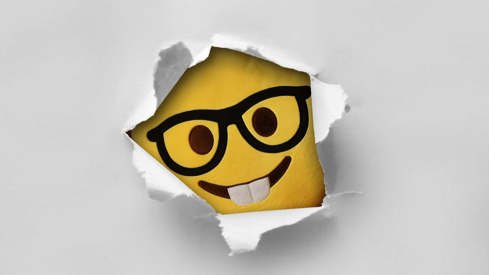Smiley 桌布 壁紙 — 一個戴眼鏡的開心黃色表情符號，從撕破的白色紙洞中偷看出來。