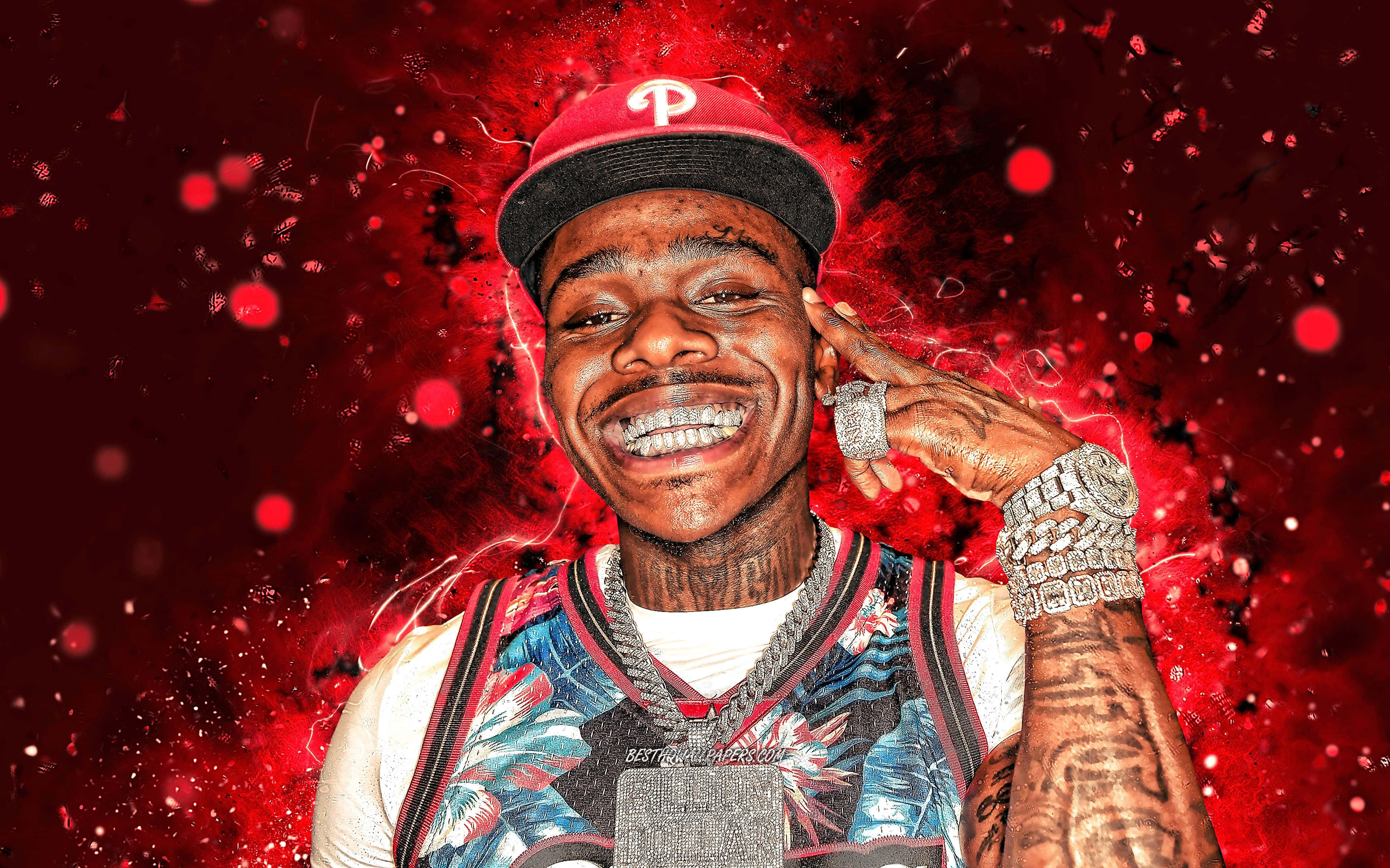 Dababy Cartoon 桌布 壁紙 — 一個戴紅帽、掛寶石鏈的微笑男子，在充滿電火花的鮮紅色潑濺背景前擺姿勢。