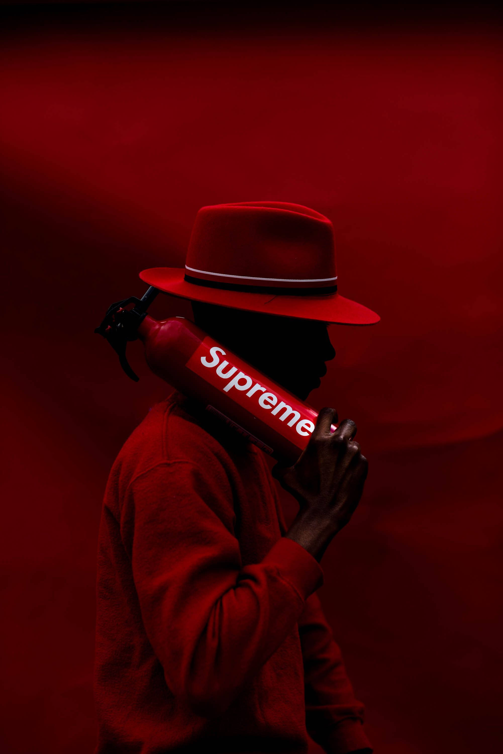 supreme aesthetic 桌布 壁紙 — 一個戴紅帽、穿紅色連帽衫的人手持紅色Supreme滅火器的剪影，背景為深紅色。