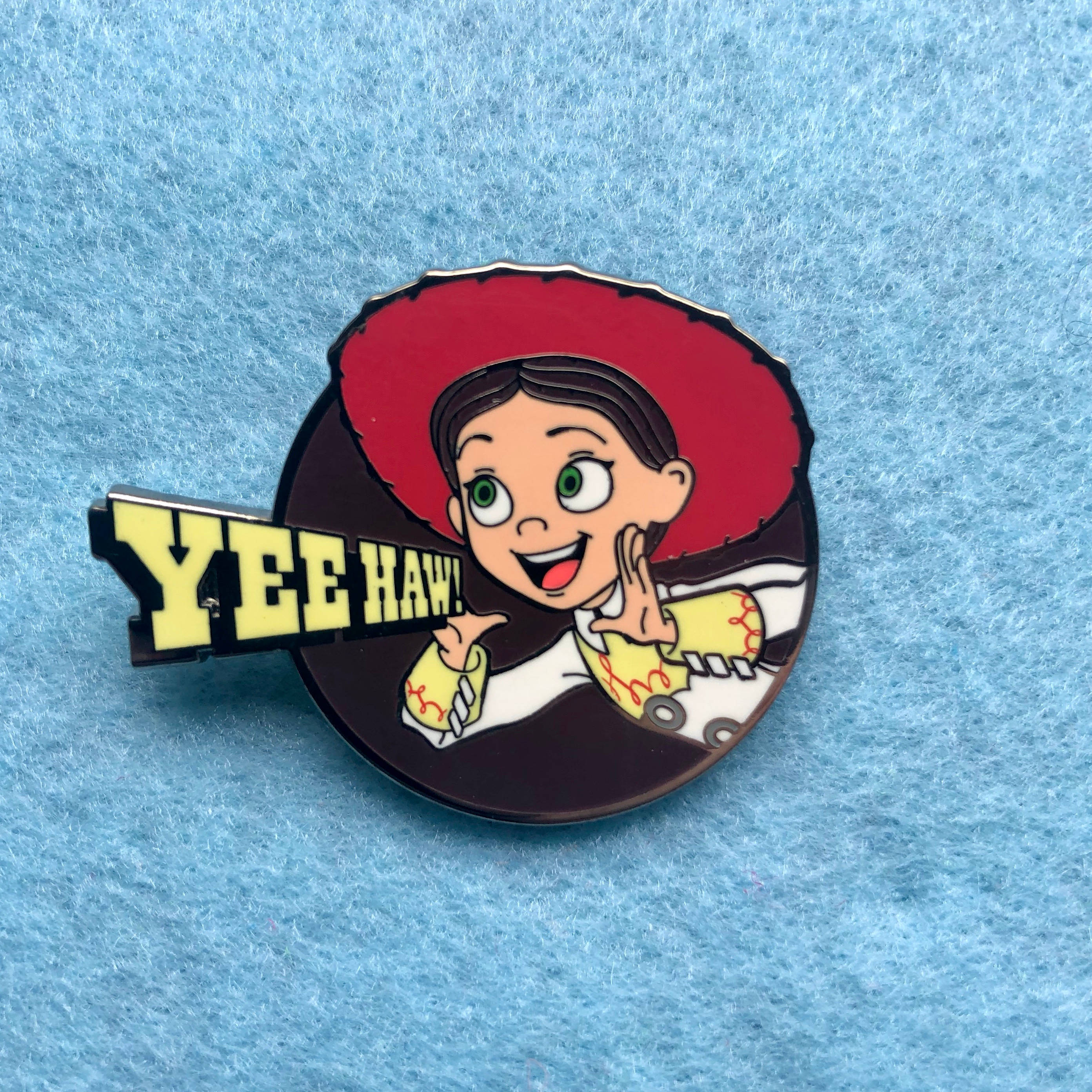 Jessie 桌布 壁紙 — 一個戴紅帽、穿黃衫的卡通女牛仔別針在藍色紋理背景上歡呼yee haw。