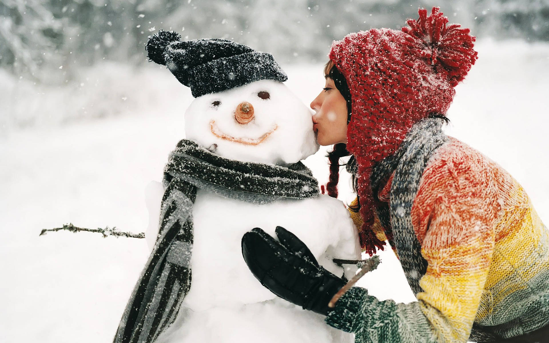 小孩在雪景中親吻雪人，身穿紅帽和彩色毛衣。 — 雪人 壁紙