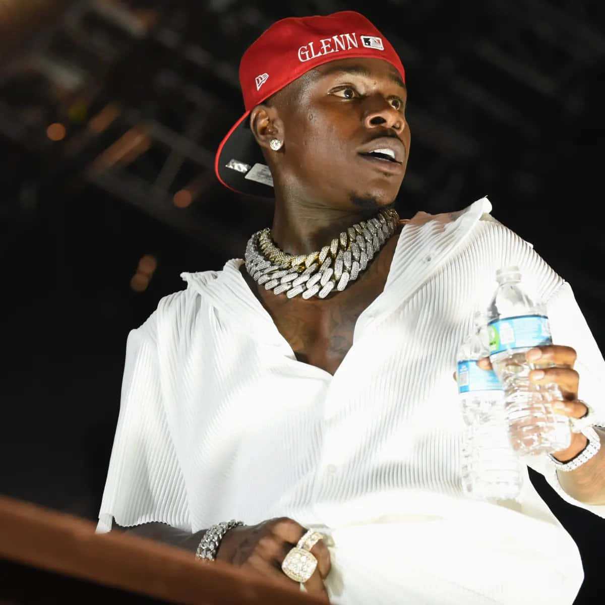 Dababy 桌布 壁紙 — 一個戴紅色帽子、穿白色褶襯衫的男人，拿著一個水瓶，同時戴著一條粗鑽石鏈和戒指。