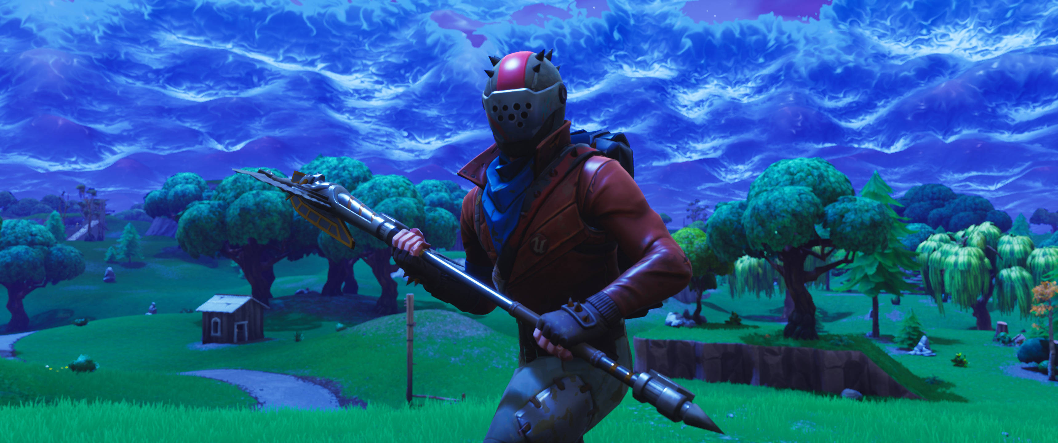 電玩遊戲 桌布 壁紙 — 一個戴紅色頭盔、穿棕色外套的Fortnite角色，在超現實的藍天、起伏的綠色山丘和樹木背景下揮舞著火箭發射器。