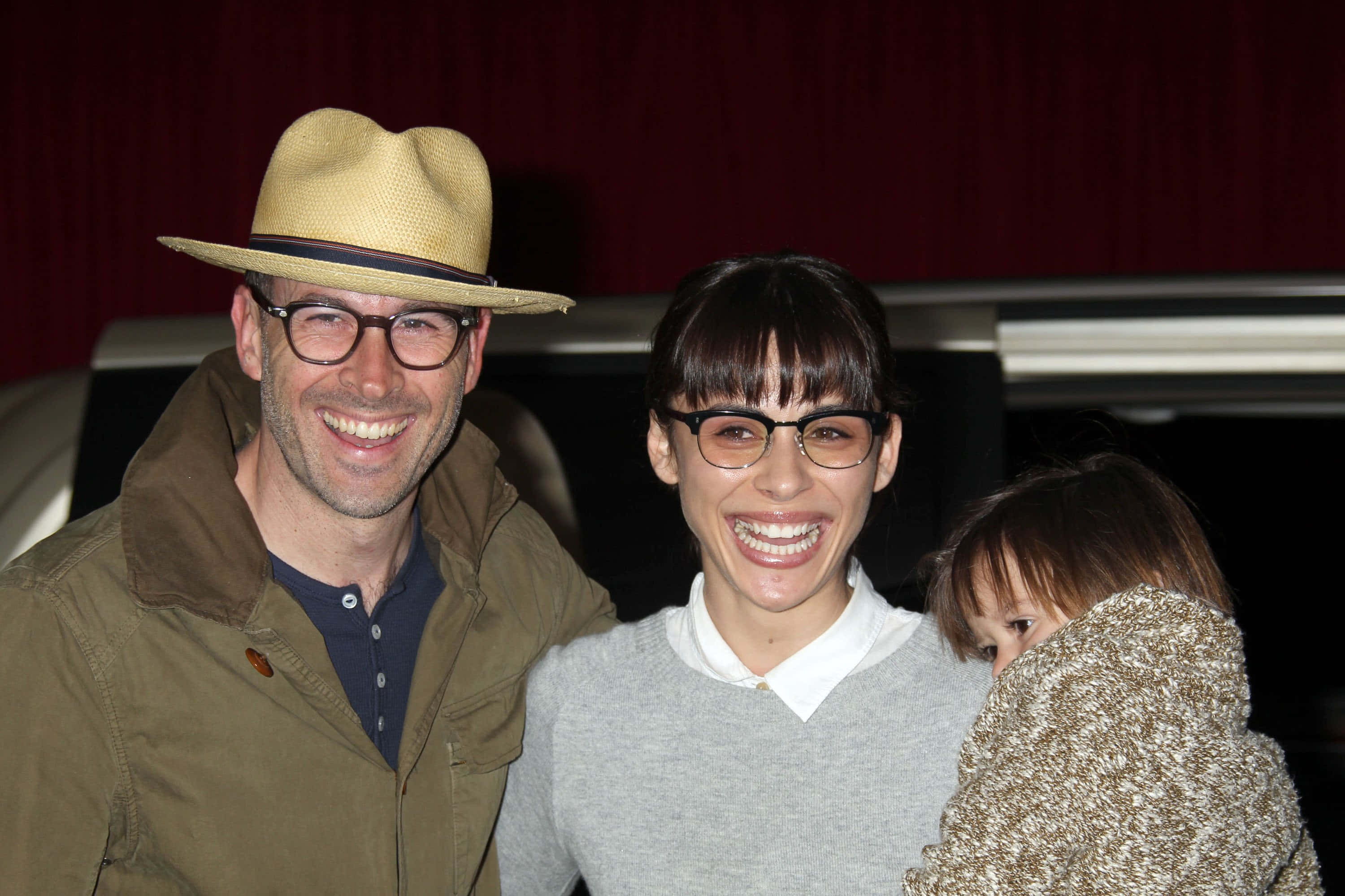 Jason Lee 桌布 壁紙 — 一個戴草帽和眼鏡的微笑男人站在一個有瀏海和眼鏡的女人旁邊，她抱著一個裹在針織毯子裡的孩子。