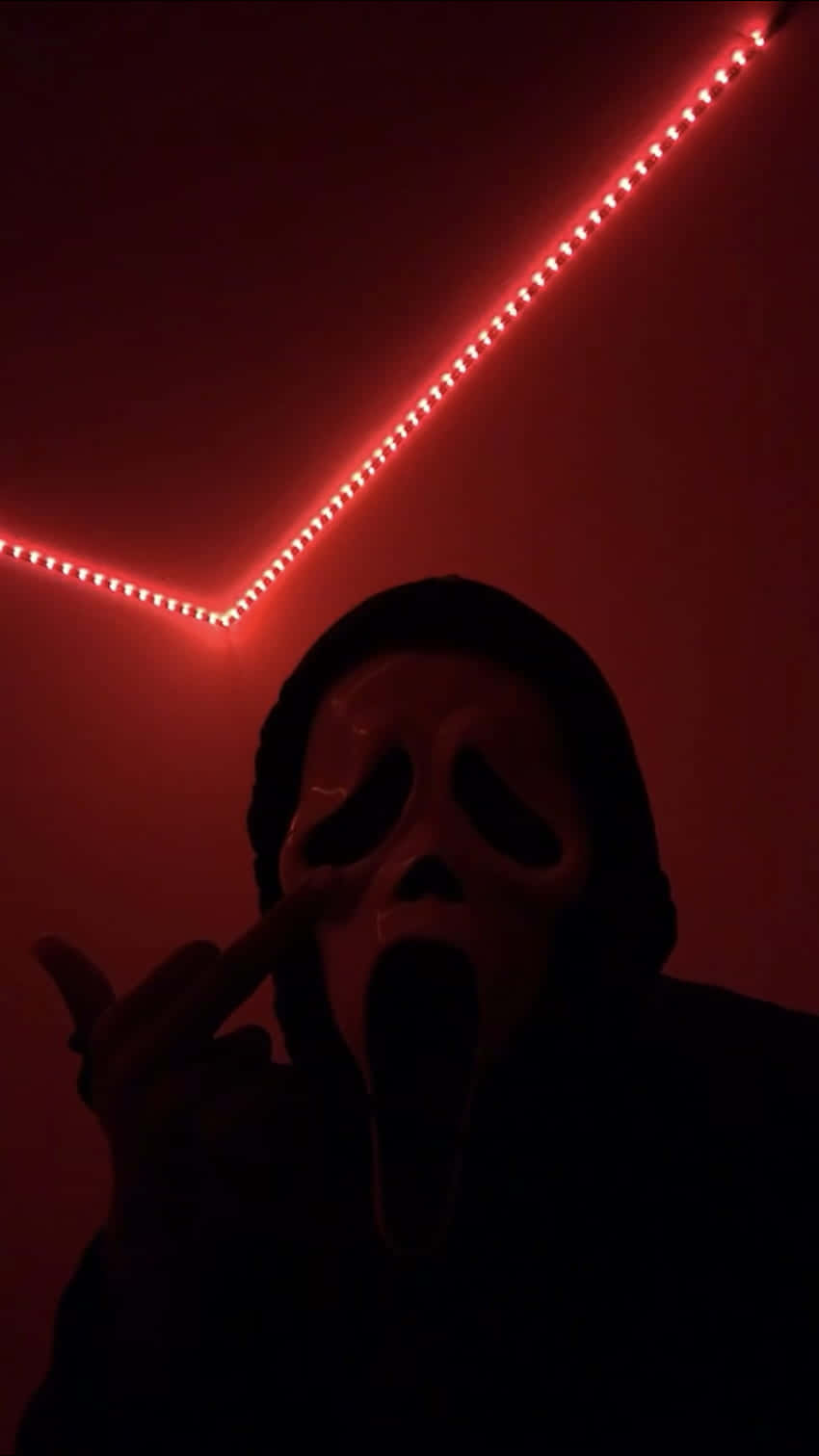 Horror Icons 桌布 壁紙 — 一個戴著Ghostface面具的人在黑暗的房間裡，在紅色LED燈下指向相機。