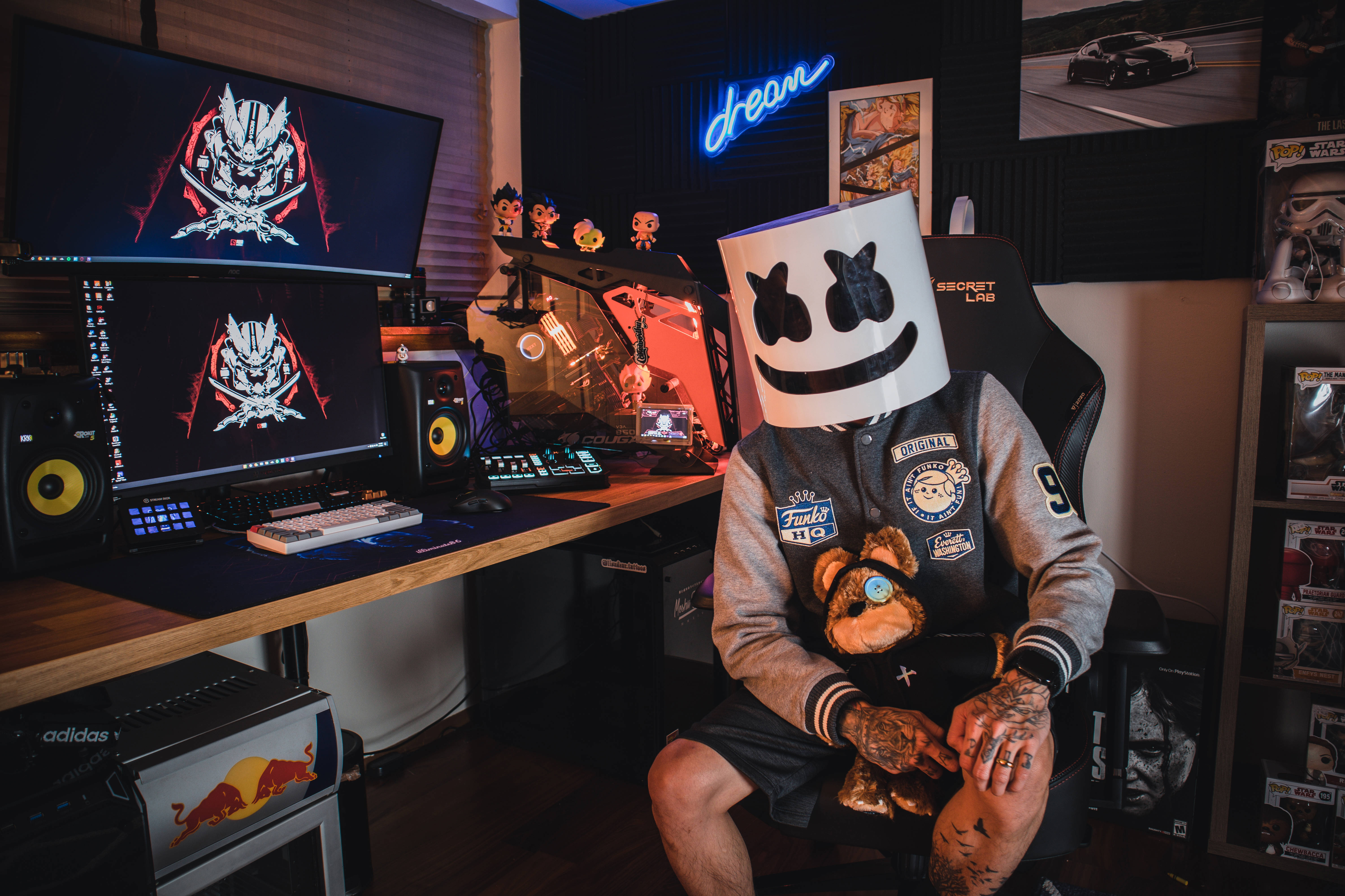 Marshmello 動態圖 桌布 壁紙 — 一個戴著Marshmello面具的人坐在電競椅上，周圍是顯示器、霓虹燈和收藏品，在昏暗的電競設置中。