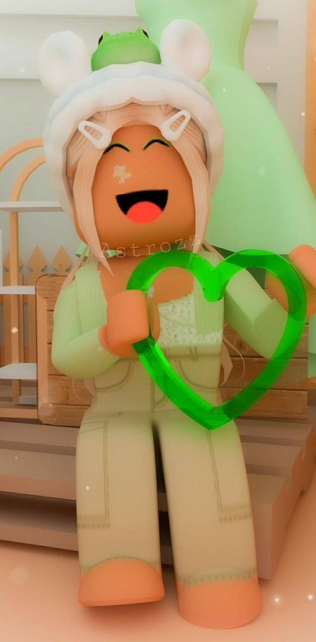 美學 Roblox 女孩 桌布 壁紙 — 一個戴著兔耳和青蛙帽的開心Roblox角色在舒適的房間裡拿著一個發光的綠色心形。