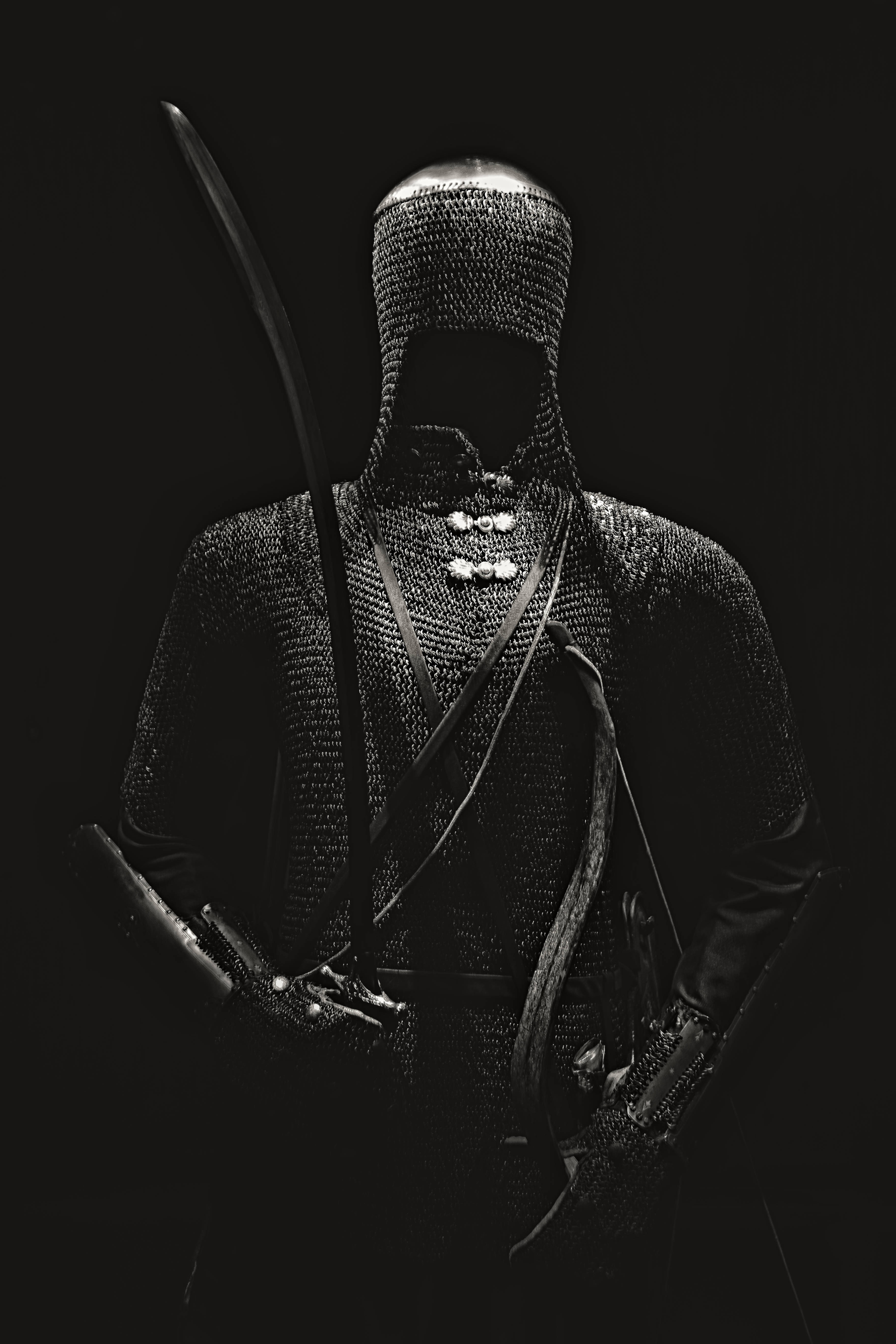 Warrior 桌布 壁紙 — 一個戴著兜帽、身穿鎖子甲的騎士，在戲劇性的單色燈光下，對著純黑背景舉劍。