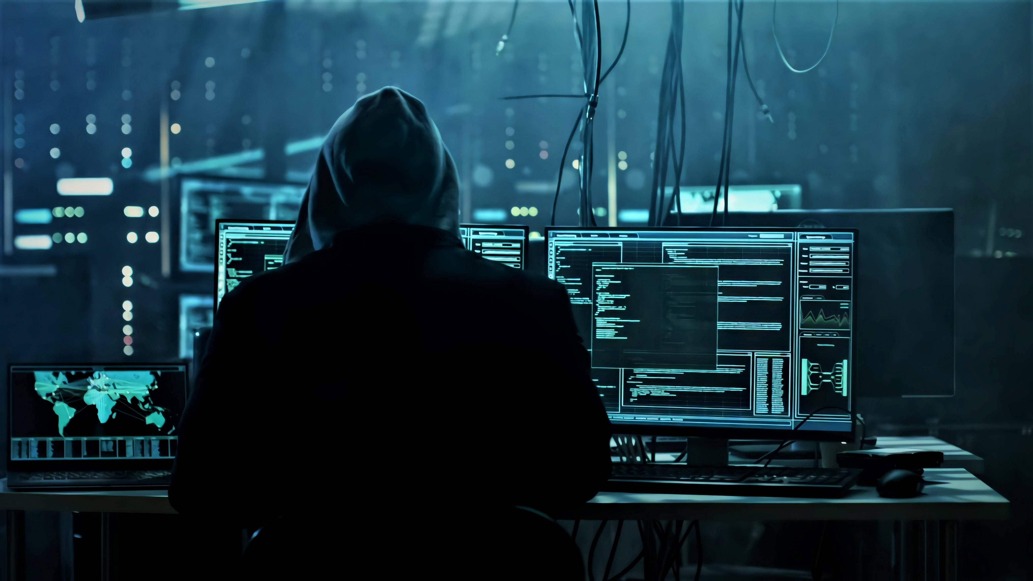 hacker 3d 桌布 壁紙 — 一個戴著兜帽的人坐在雜亂的辦公桌前，周圍是發光的電腦螢幕，顯示著程式碼和世界地圖，身處昏暗的伺服器機房。