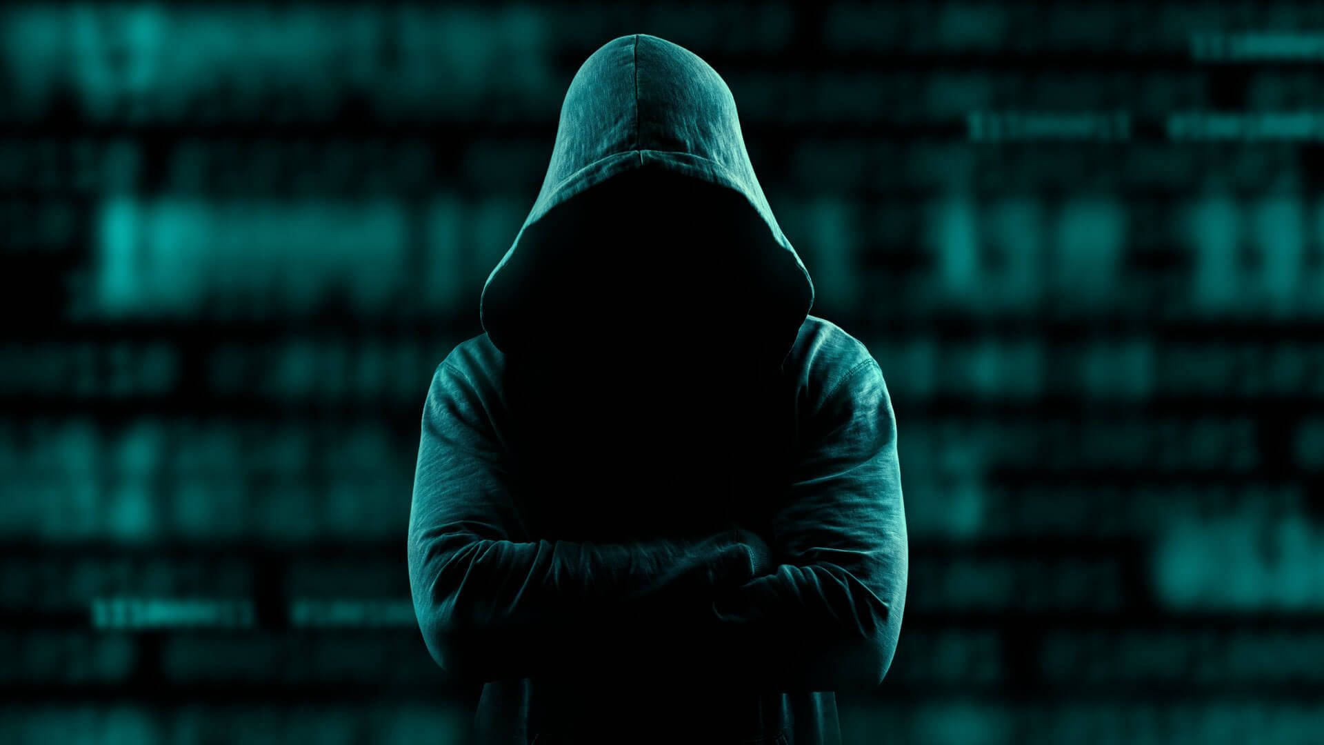 Hacker Full HD 桌布 壁紙 — 一個戴著兜帽的人物交叉雙臂站立，背景是青綠色的數位代碼，臉部隱藏在陰影中。