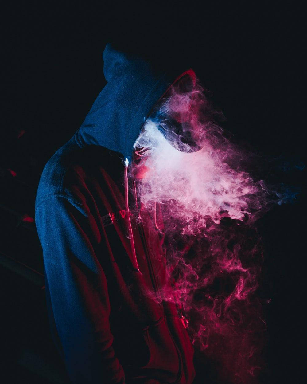 neon aesthetic iPhone 桌布 壁紙 — 一個戴著兜帽的人物在藍色和紅色霓虹燈照亮的黑暗背景下呼出充滿活力的粉紅色煙霧。