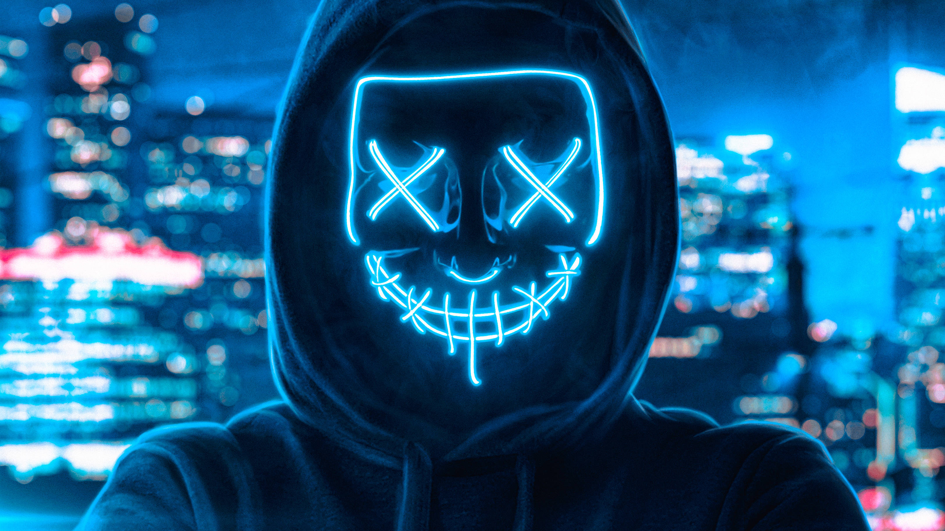 Mask 桌布 壁紙 — 一個戴著兜帽的人物戴著發光藍色LED面具，有X形眼睛和縫合的笑容，背景是模糊的霓虹城市夜景。