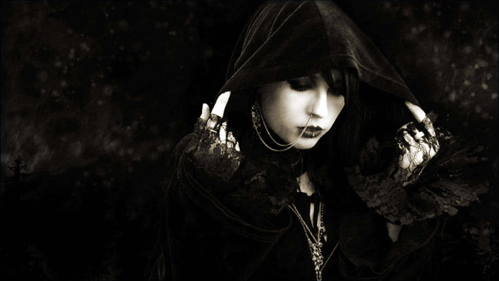 Goth Aesthetic Black 桌布 壁紙 — 一個戴著兜帽的哥德式人物，蒼白的妝容和華麗的手套，在黑暗的氛圍中向下凝視。