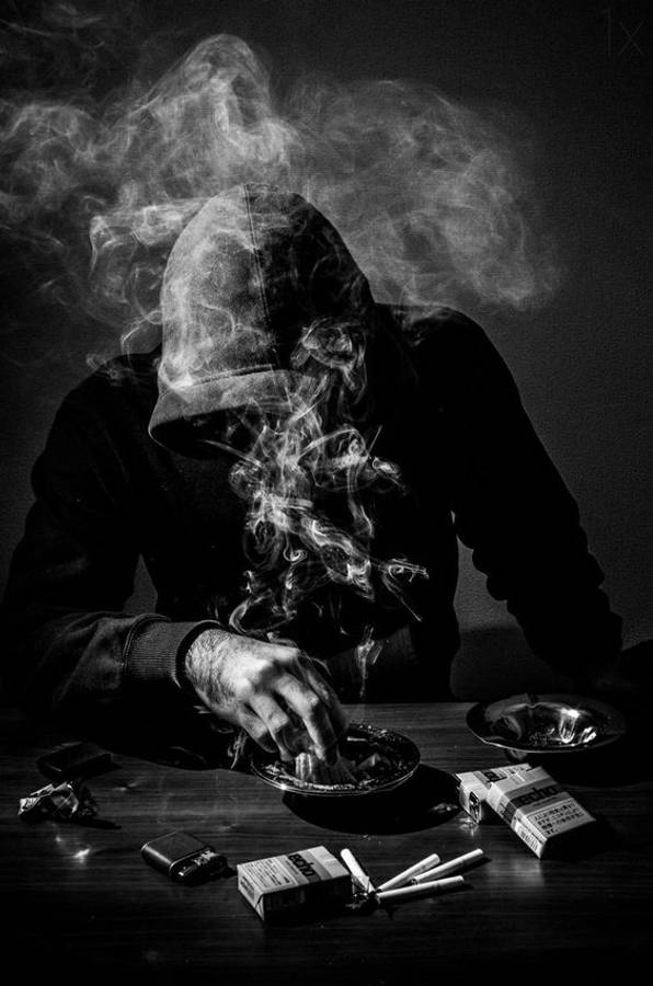 bad 桌布 壁紙 — 一個戴著兜帽的身影在昏暗的房間裡抽煙，煙霧在他們模糊的臉龐周圍旋轉。