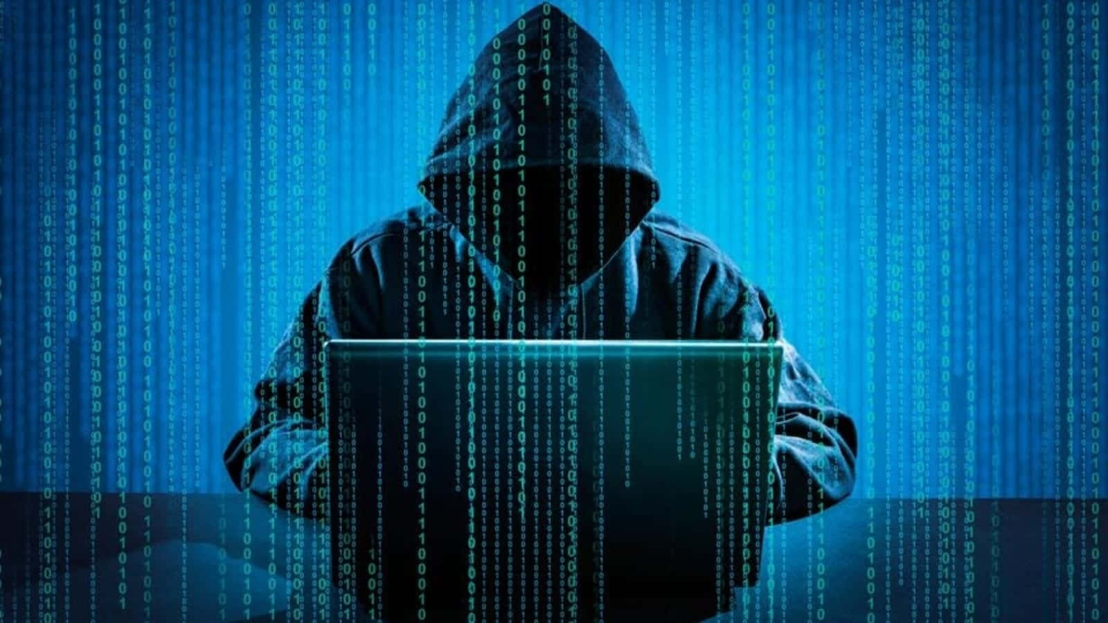 Vulnerable 桌布 壁紙 — 一個戴著兜帽的身影坐在發光的筆記型電腦前，綠色二進制代碼如數位風暴般傾瀉而下。