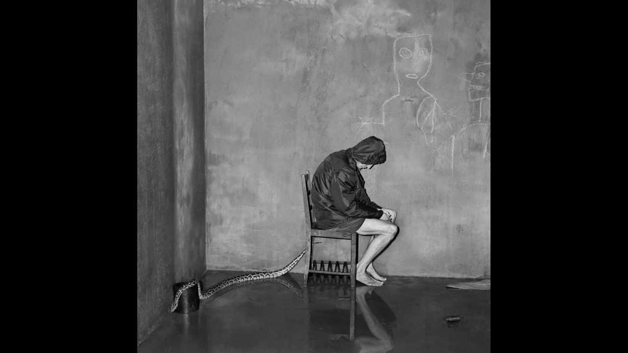 Scary Black And White 桌布 壁紙 — 一個戴著兜帽的身影獨自坐在一張椅子上，房間空無一物，牆上有粉筆畫，一條蛇從水桶下爬出來。