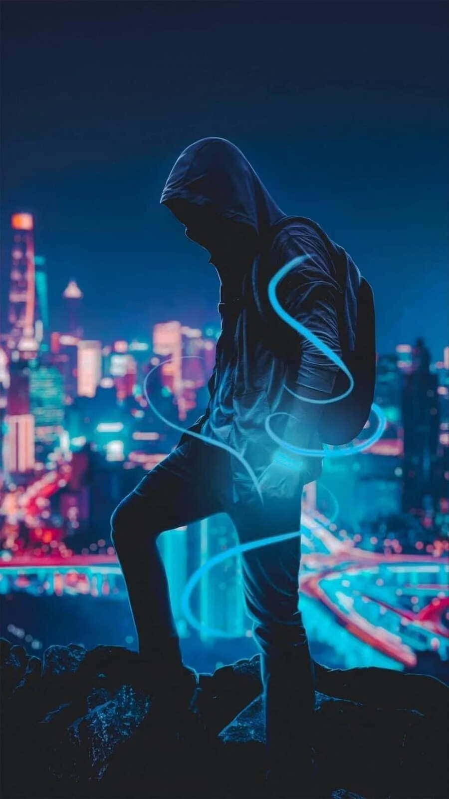  壁紙 — 一個戴著兜帽的身影站在岩石露頭上，俯瞰著夜晚充滿活力的霓虹燈城市景觀，周圍環繞著發光的藍色能量漩渦。