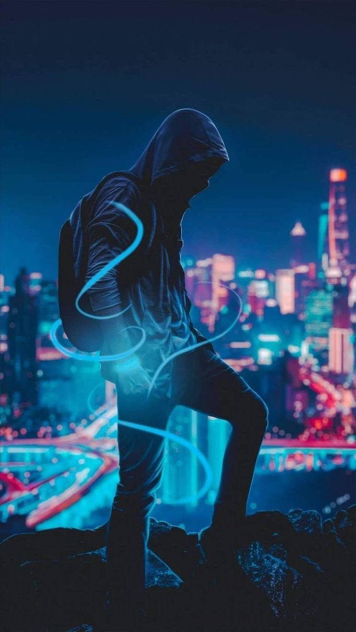 時尚 桌布 壁紙 — 一個戴著兜帽的身影站在岩石露頭上，俯瞰著夜晚充滿活力的霓虹燈城市景觀，周圍環繞著發光的藍色能量漩渦。