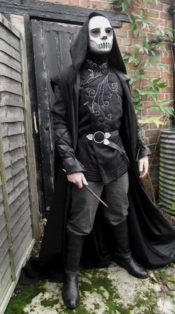 Death Eaters 桌布 壁紙 — 一個戴著全黑骷髏面具和連帽斗篷的人站在一扇風化的木門前，地上有綠色苔蘚。