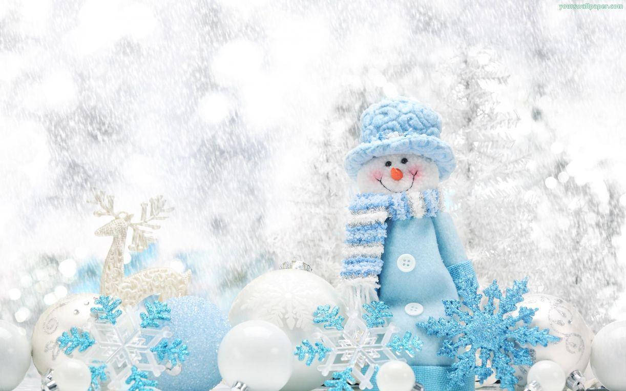 Cute Snow 桌布 壁紙 — 一個戴著圍巾和帽子的歡樂藍色針織雪人，站在閃爍的雪花和裝飾品之間，背景是雪地。