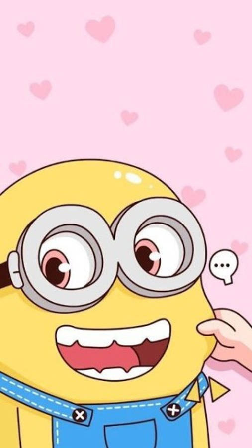 小黃人 桌布 壁紙 — 一個戴著大護目鏡、咧嘴大笑的開心黃色Minion，在粉紅色心形圖案背景上被一隻手頑皮地觸摸。