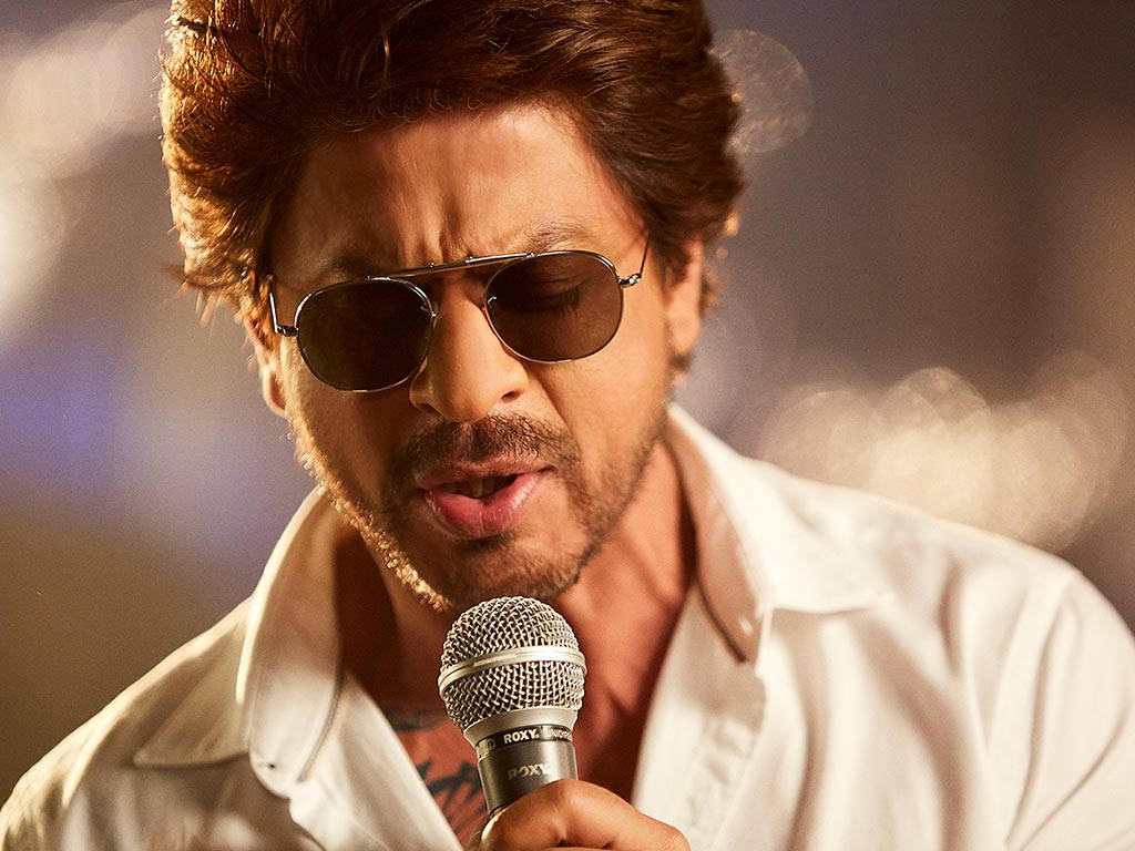 Shahrukh 桌布 壁紙 — 一個戴著太陽眼鏡、身穿白色襯衫的男人，在模糊的散景背景下，對著麥克風激情演唱。
