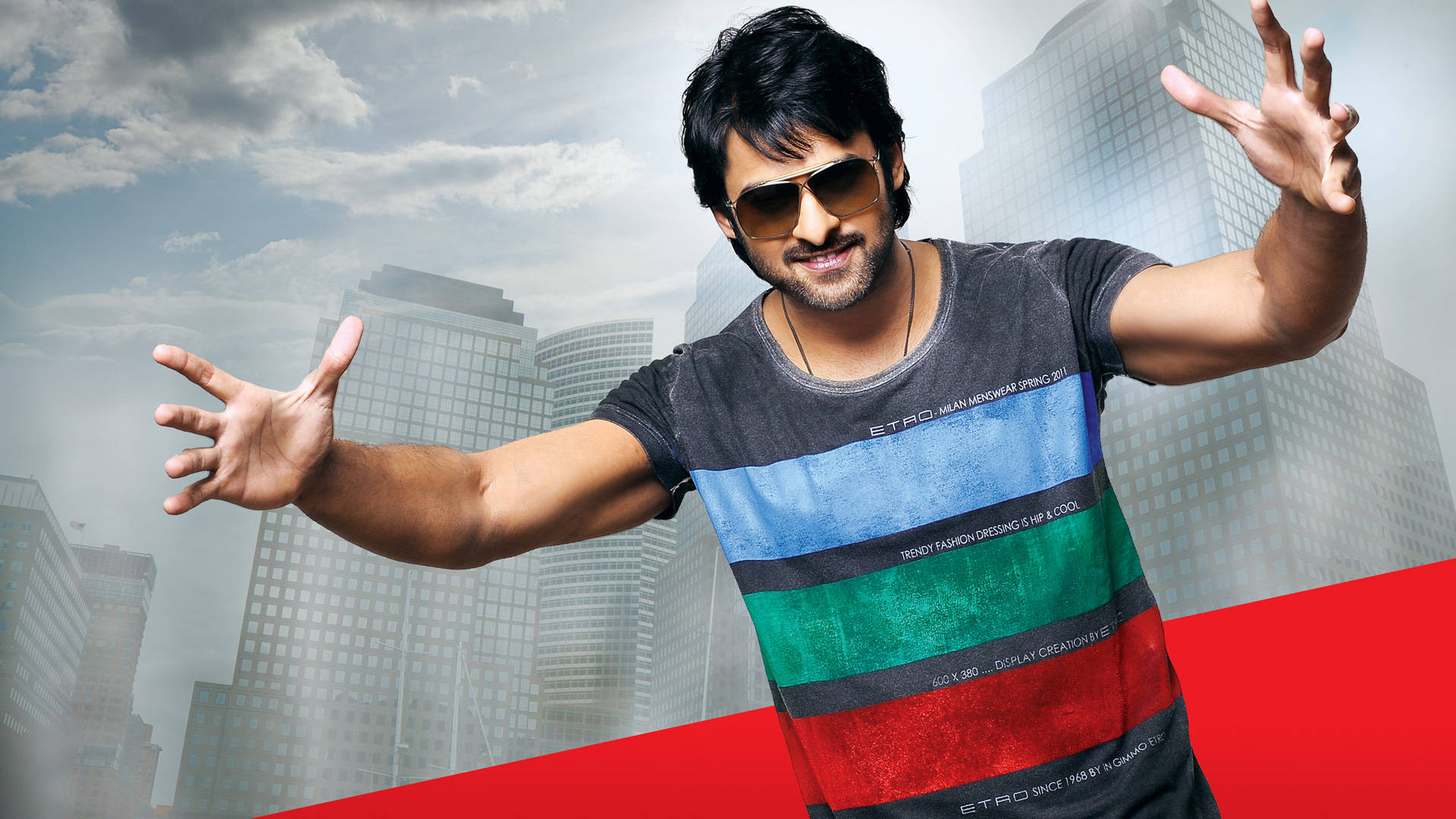 Prabhas HD 桌布 壁紙 — 一個戴著太陽眼鏡和條紋襯衫的男人，在模糊的城市天際線和醒目的紅色對角線條前擺出動態姿勢。