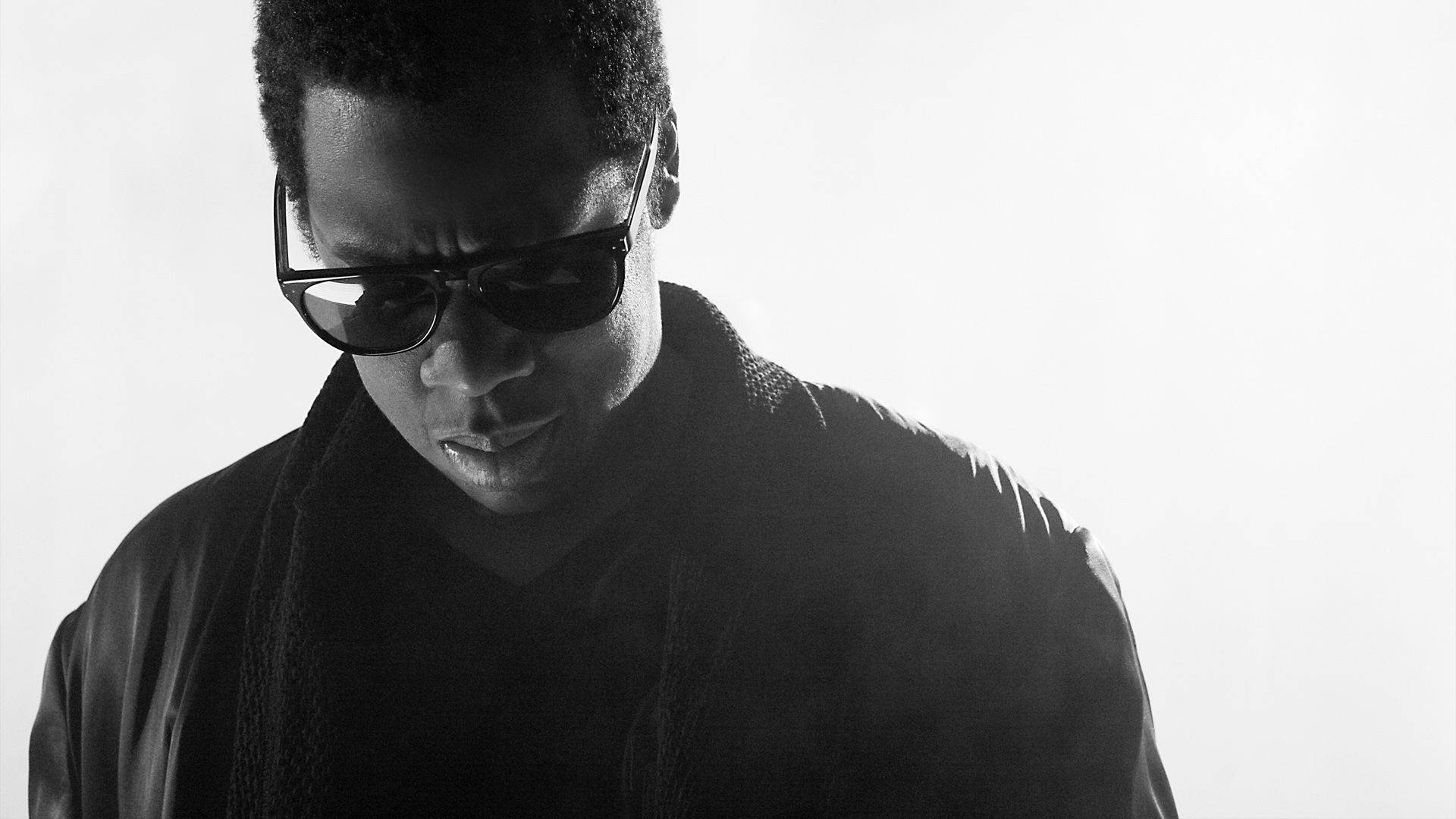 Jay-z 桌布 壁紙 — 一個戴著太陽眼鏡和深色外套的男人，在純白背景上以高對比黑白影像向下凝視。