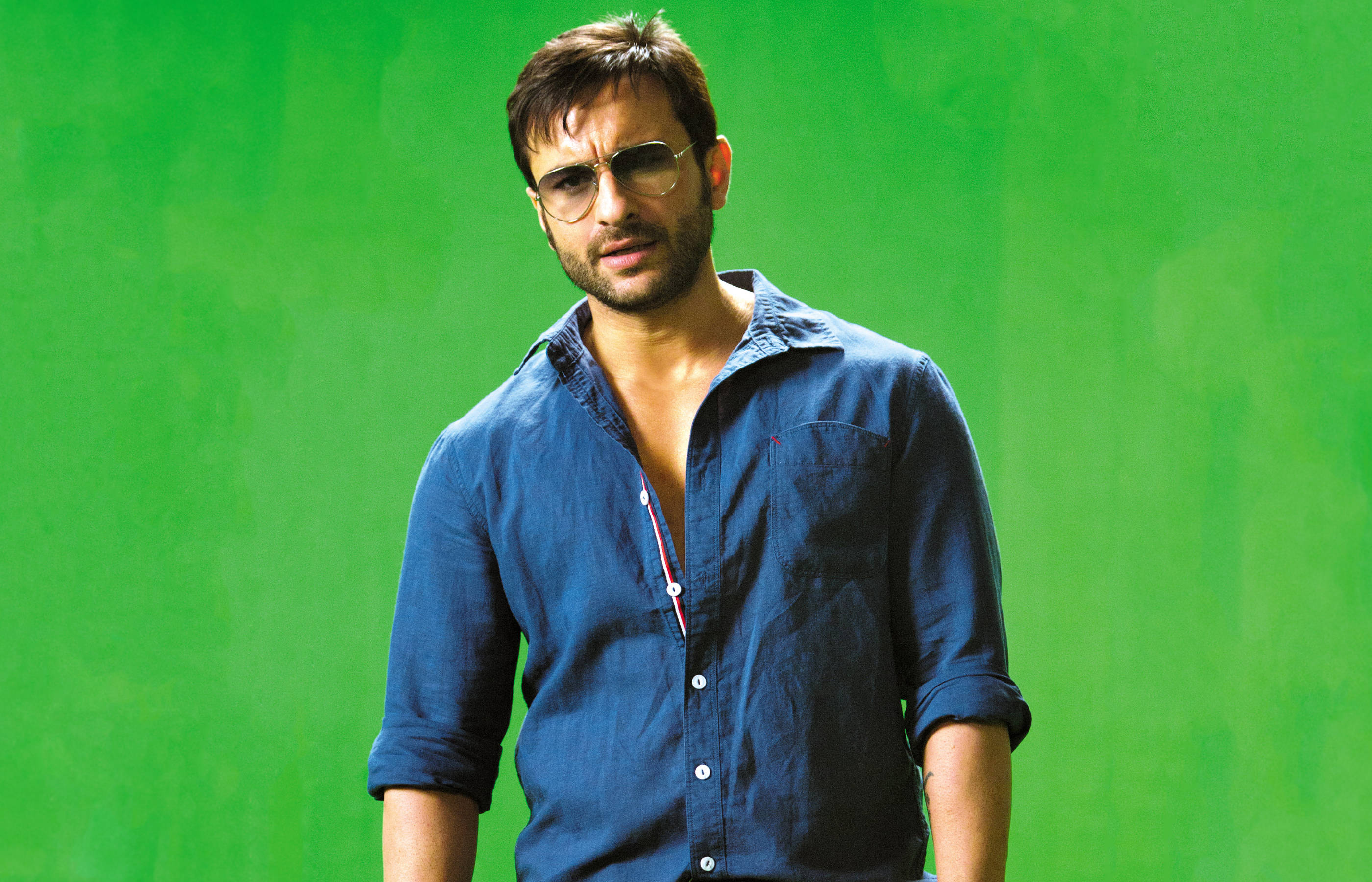 Saif Ali Khan 桌布 壁紙 — 一個戴著太陽眼鏡和藍色襯衫的男人自信地站在純綠色螢幕背景前。