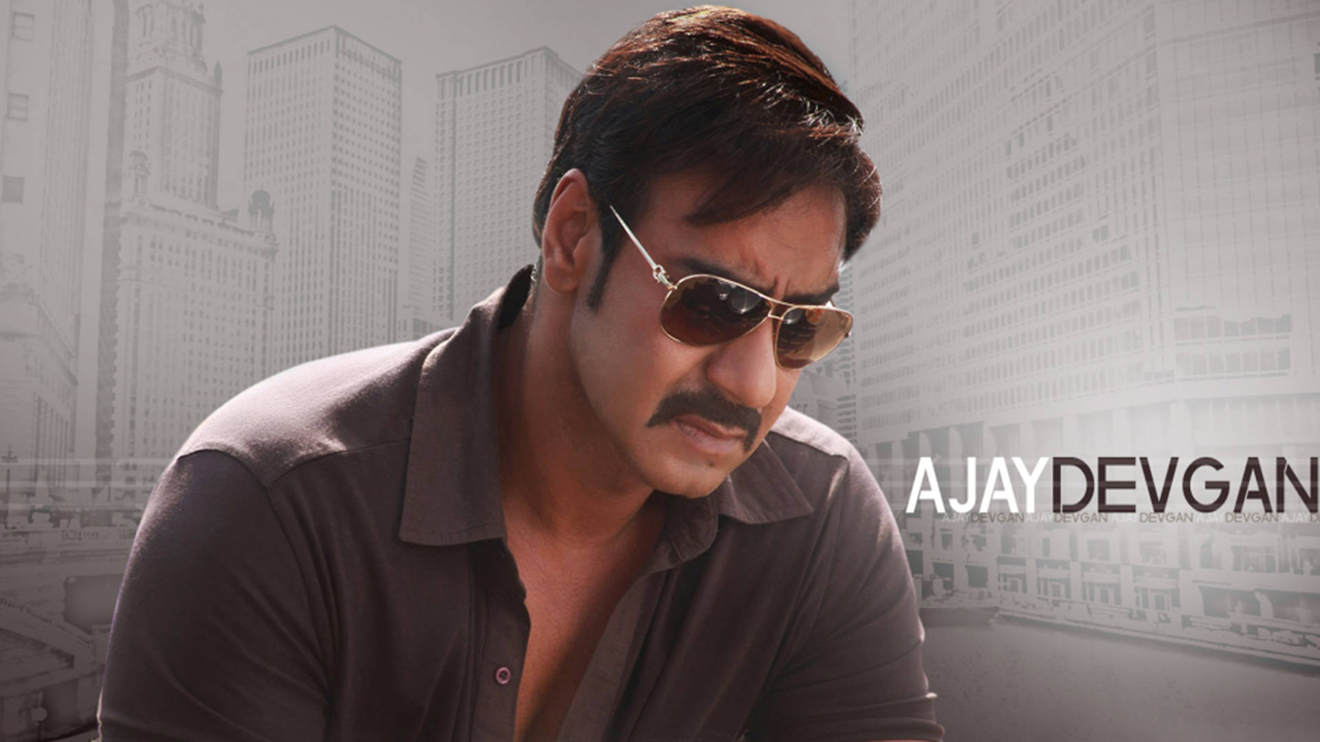 ajay devgn 桌布 壁紙 — 一個戴著太陽眼鏡和鬍子的男人，在模糊的城市天際線背景下專注地凝視。