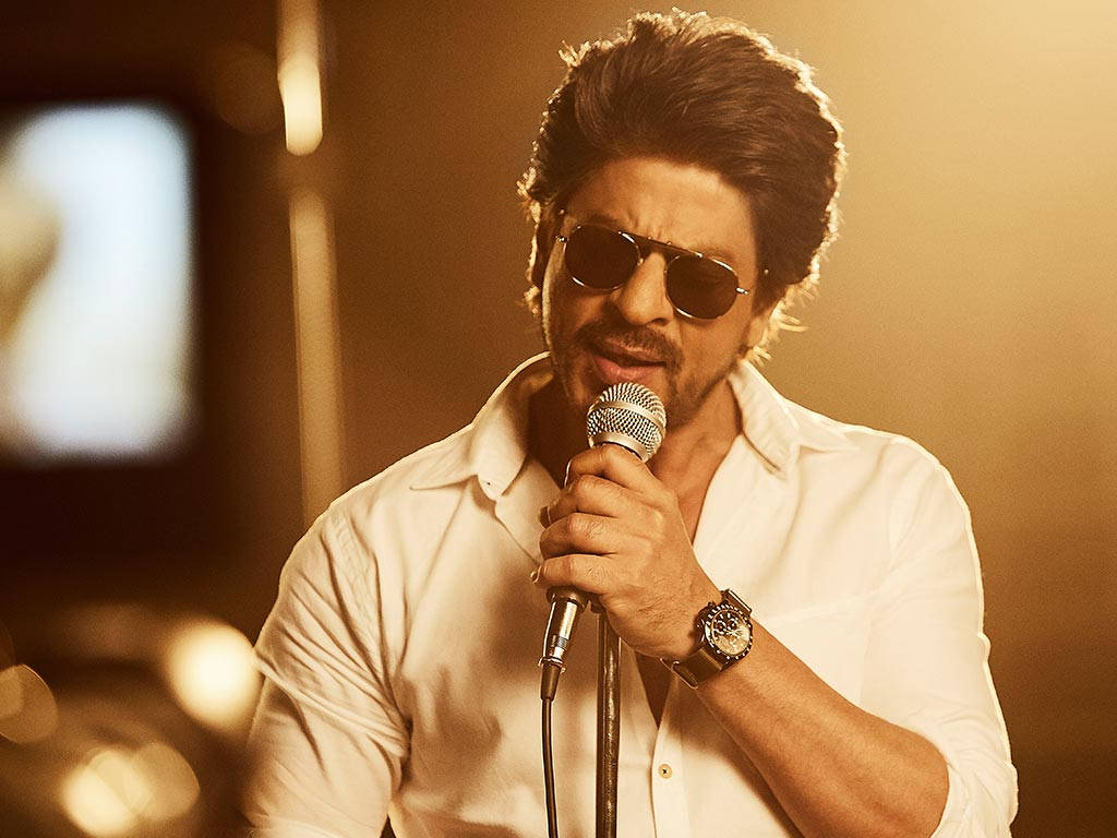 Shahrukh 桌布 壁紙 — 一個戴著太陽眼鏡的男人在溫暖的金色舞台燈光下對著麥克風唱歌。