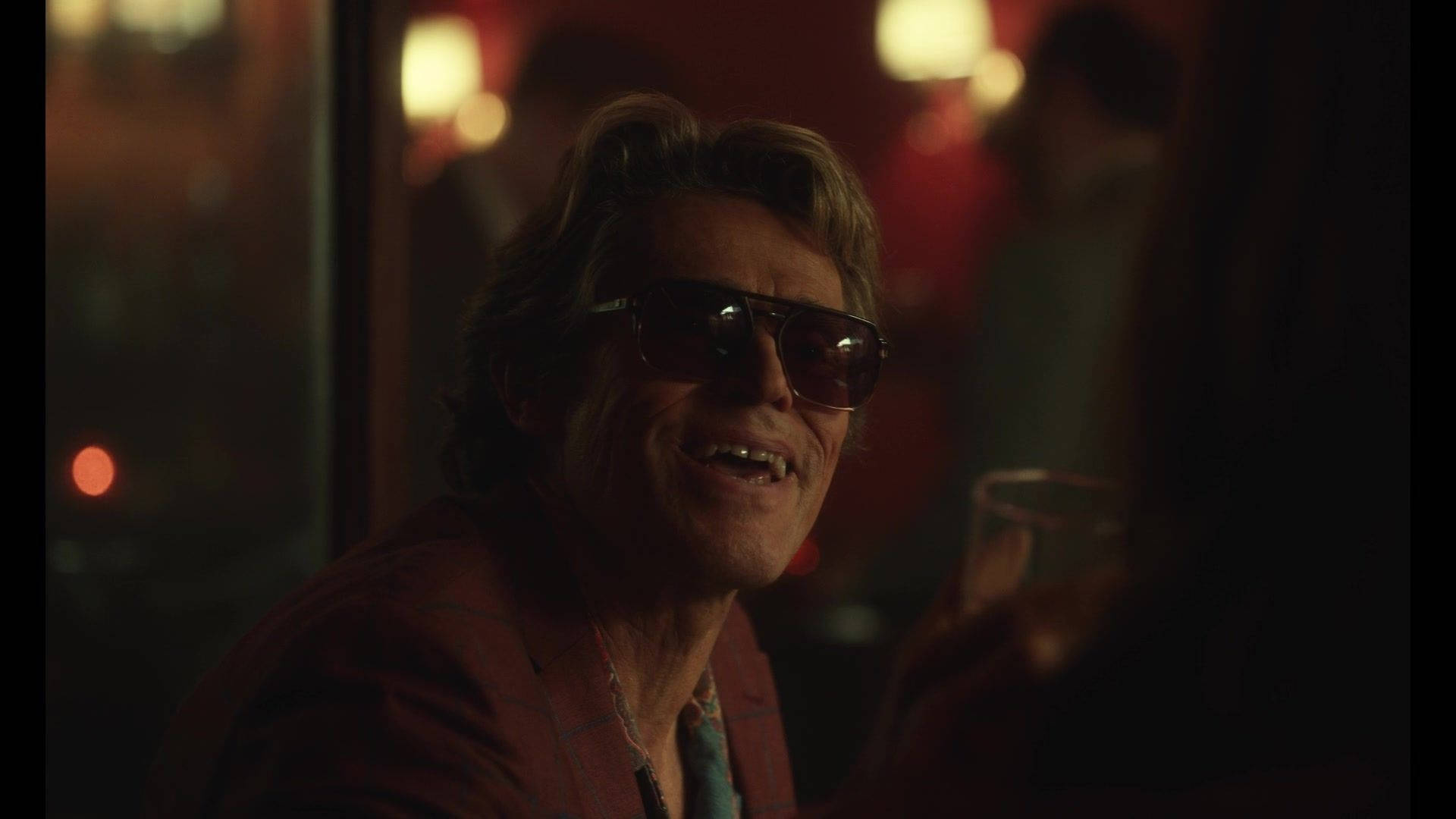 Willem Dafoe 桌布 壁紙 — 一個戴著太陽眼鏡的男人在燈光昏暗、背景有柔和燈光的酒吧裡溫暖地微笑。