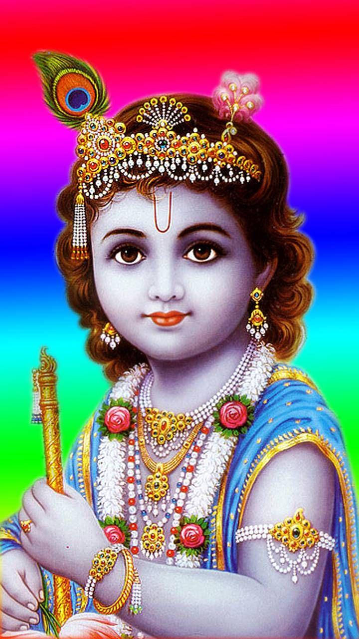 krishna phone 桌布 壁紙 — 一個戴著孔雀羽毛皇冠和金色飾品的神聖小孩，在充滿活力的彩虹漸變背景前拿著一支笛子。