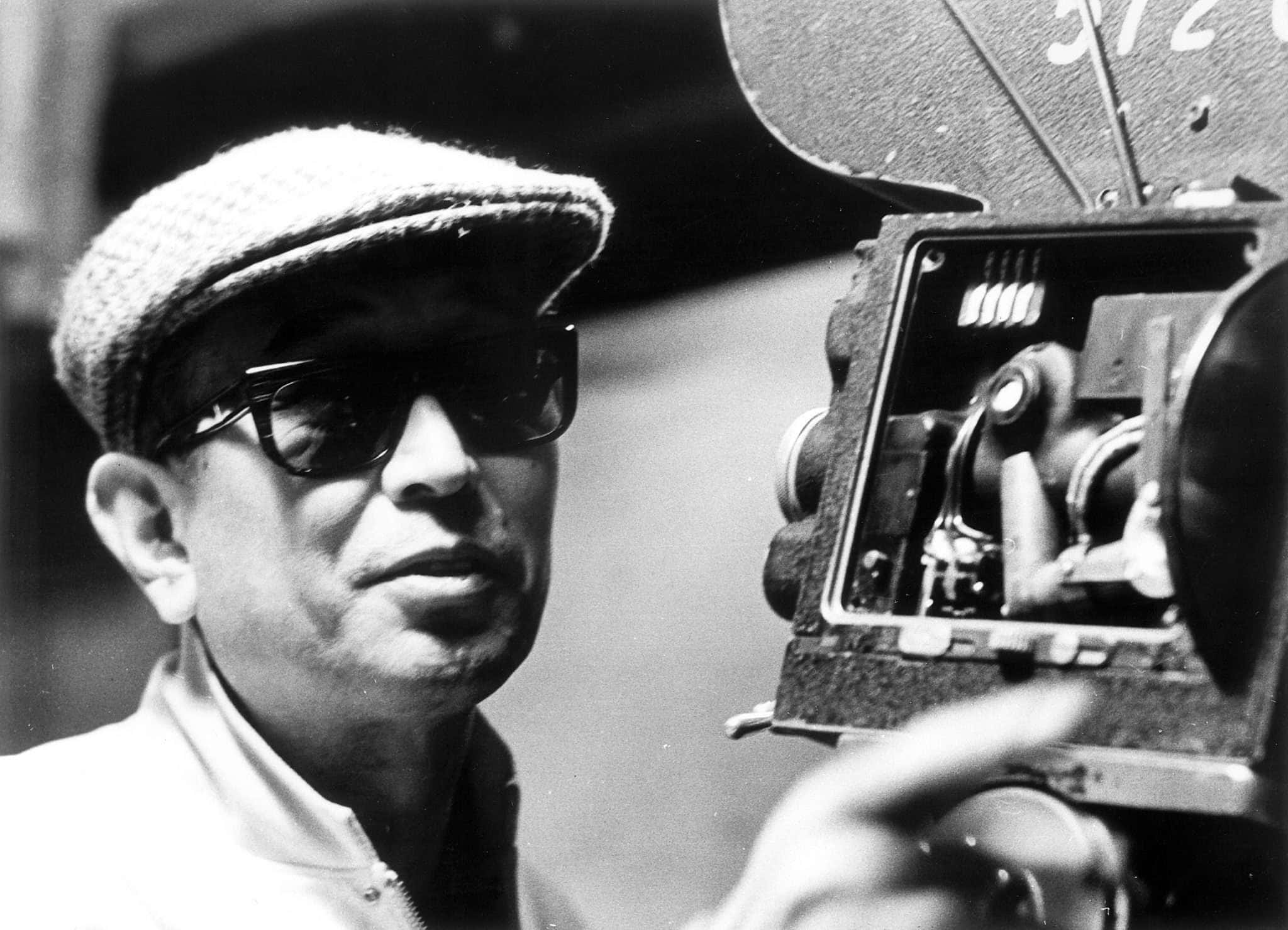 Akira Kurosawa 桌布 壁紙 — 一個戴著帽子和太陽眼鏡的男人操作復古底片相機的黑白肖像。