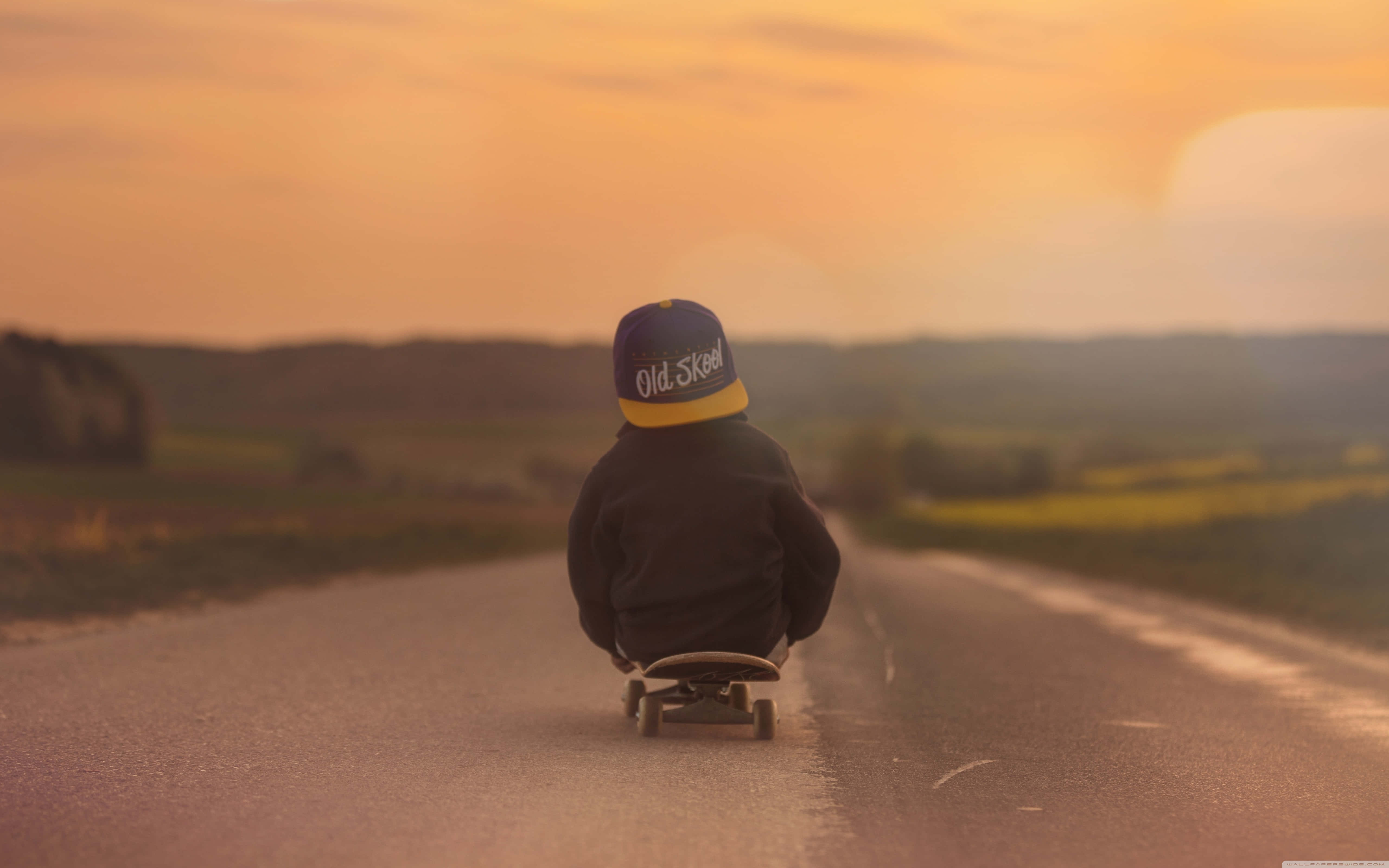 Retro Skateboard 桌布 壁紙 — 一個戴著帽子的孩子在一條被金色夕陽照亮的鄉村道路上玩滑板。