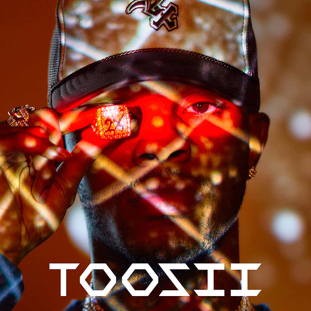 Toosii 桌布 壁紙 — 一個戴著帽子的男人，在溫暖模糊的背景前，將一顆發光的紅色寶石舉到眼前。