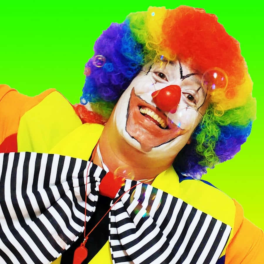 搞笑 桌布 壁紙 — 一個戴著彩虹假髮和紅鼻子的快樂小丑，在帶有浮動氣泡的亮綠色背景上微笑。