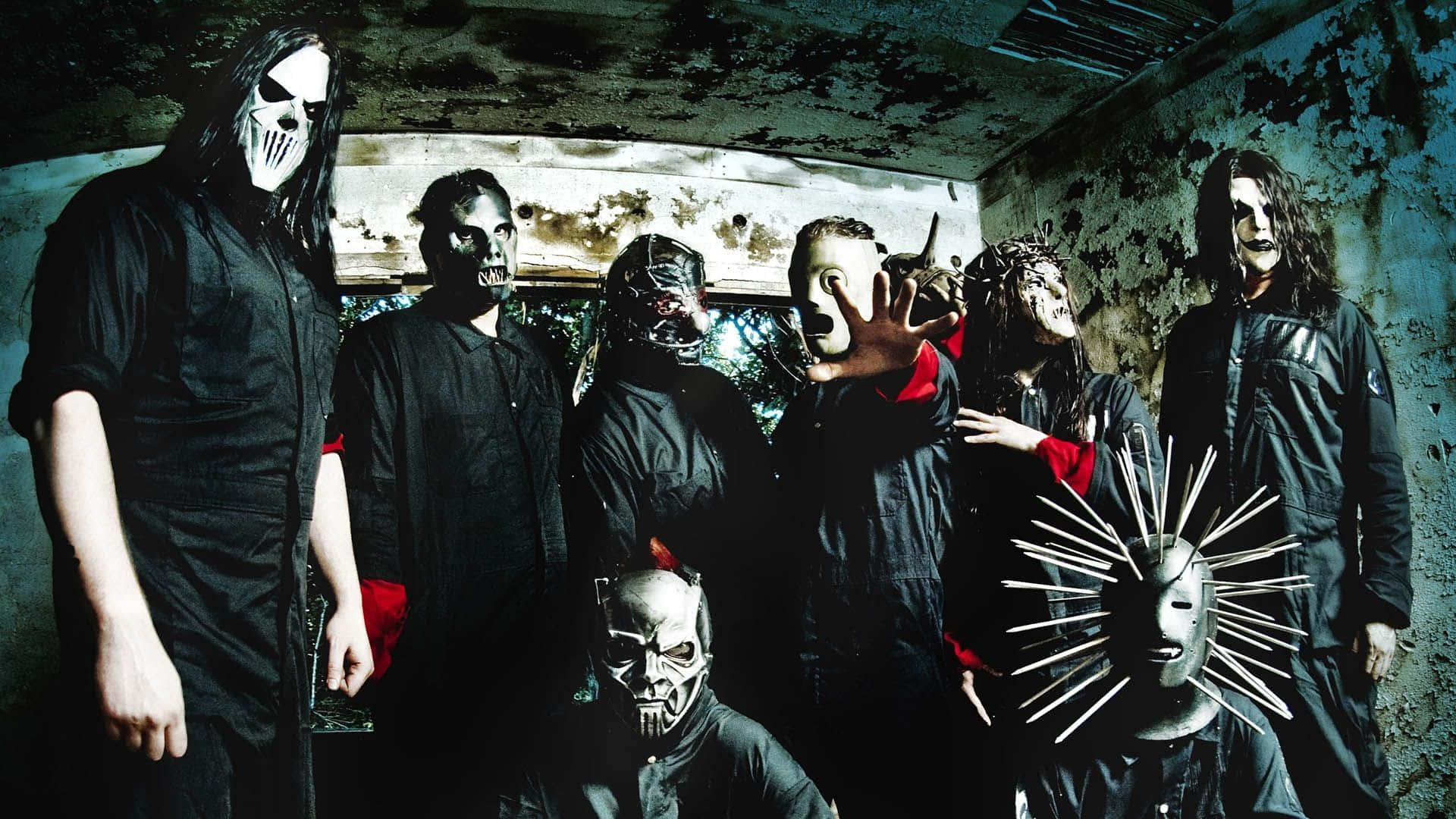 Slipknot 桌布 壁紙 — 一個戴著怪誕面具的樂隊在一個牆壁剝落、天花板破損的腐朽發霉房間裡擺出威脅性的姿勢。