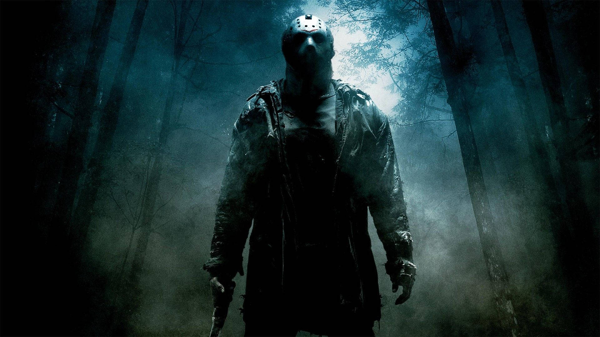 horror villains 桌布 壁紙 — 一個戴著曲棍球面具的威脅人物站在迷霧籠罩的黑暗森林中，伴隨著詭異的藍色燈光。
