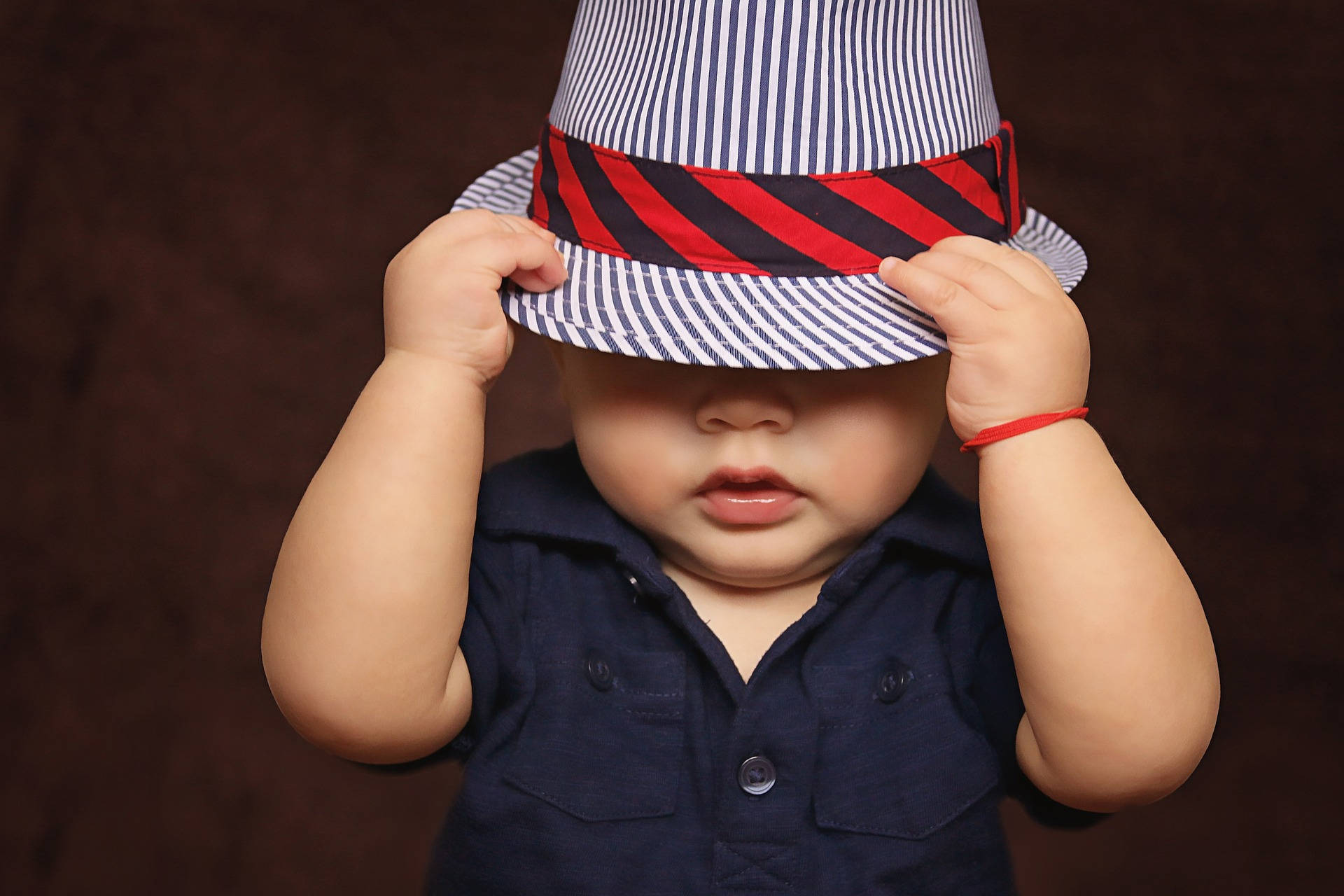 Very Cute Baby 桌布 壁紙 — 一個戴著條紋帽子的嬰兒把帽子拉低，遮住眼睛，背景是深棕色。