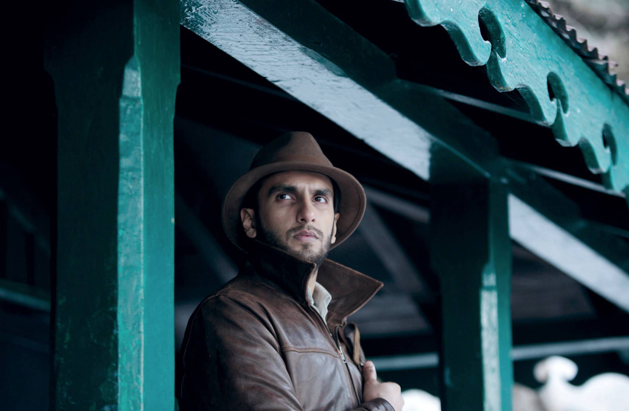 Ranveer Singh 桌布 壁紙 — 一個戴著棕色軟呢帽、身穿皮夾克的男人，在飽經風霜的綠色木簷下若有所思地凝視。