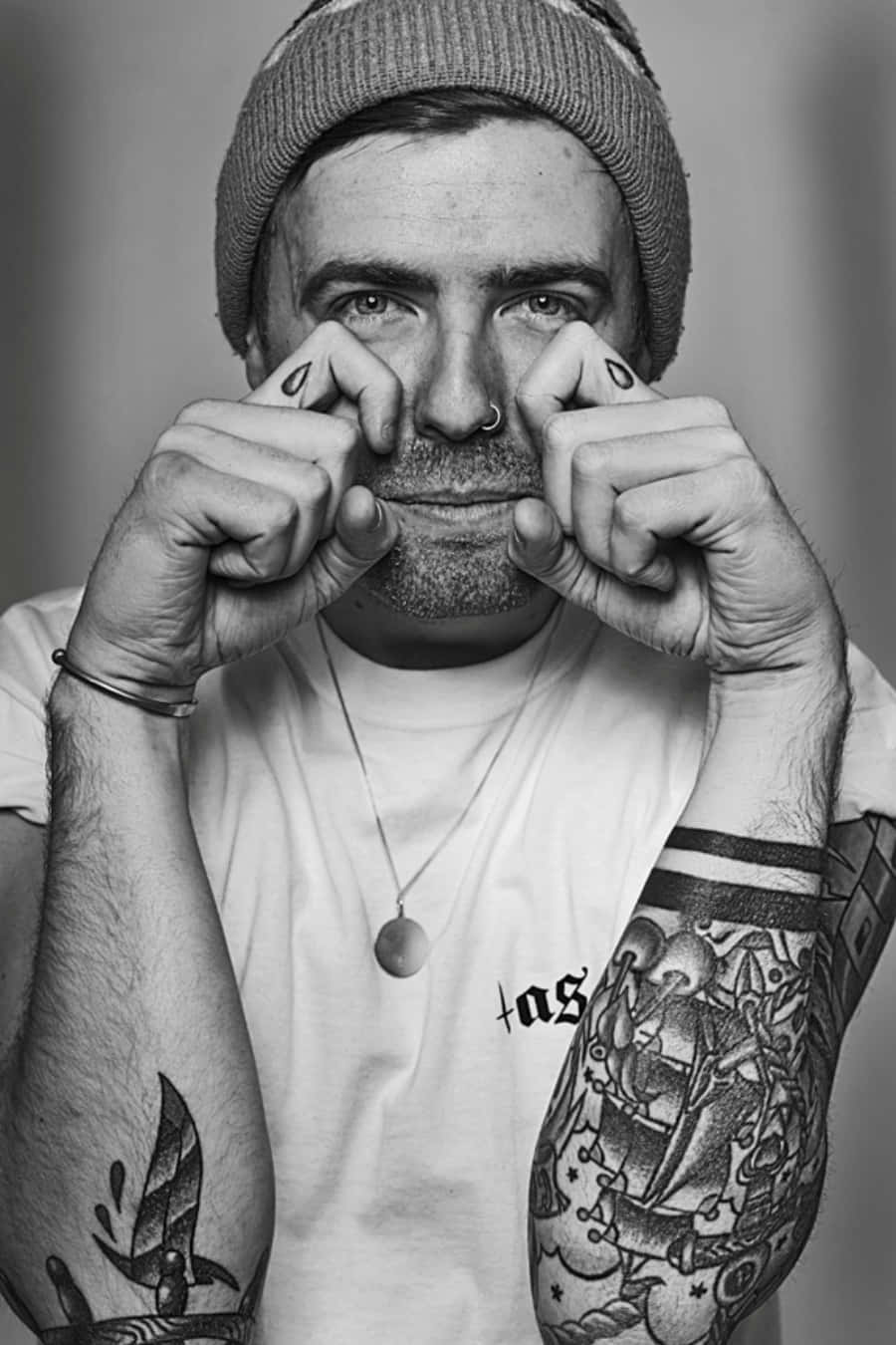 Tattoo Boy 桌布 壁紙 — 一個戴著毛帽、有刺青的男人，頑皮地捏著鼻子，眼神銳利的黑白肖像。
