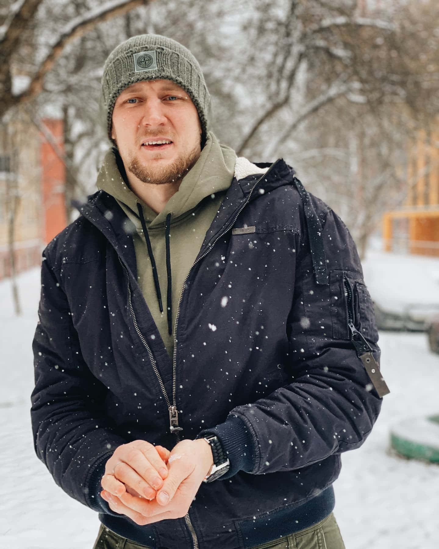 Celebrity 桌布 壁紙 — 一個戴著毛帽和冬季外套的男人站在飄雪中，背後是光禿的樹木和積雪覆蓋的地面。